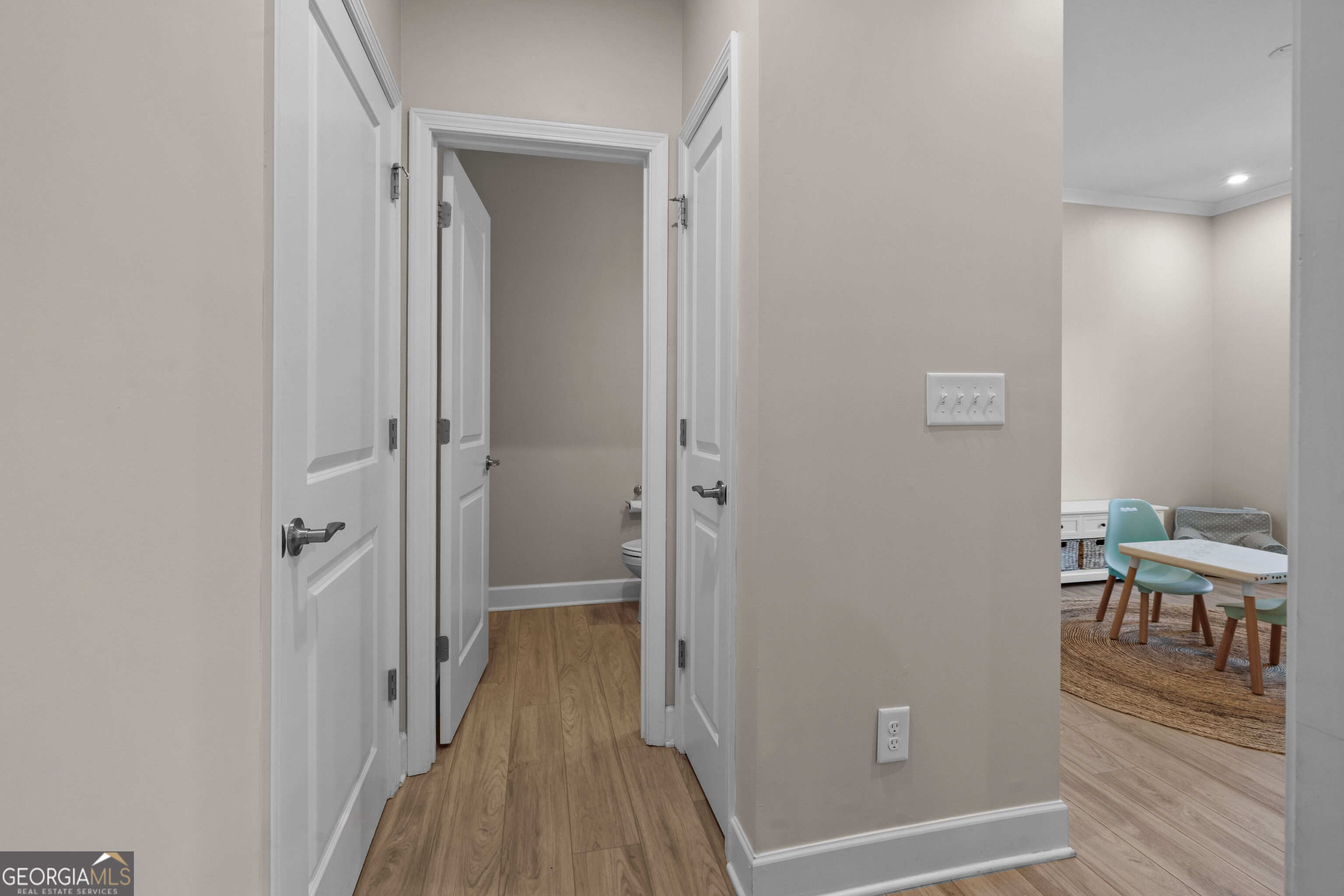 Wood-floored hallway with open doors to a bathroom and a furnished playroom.