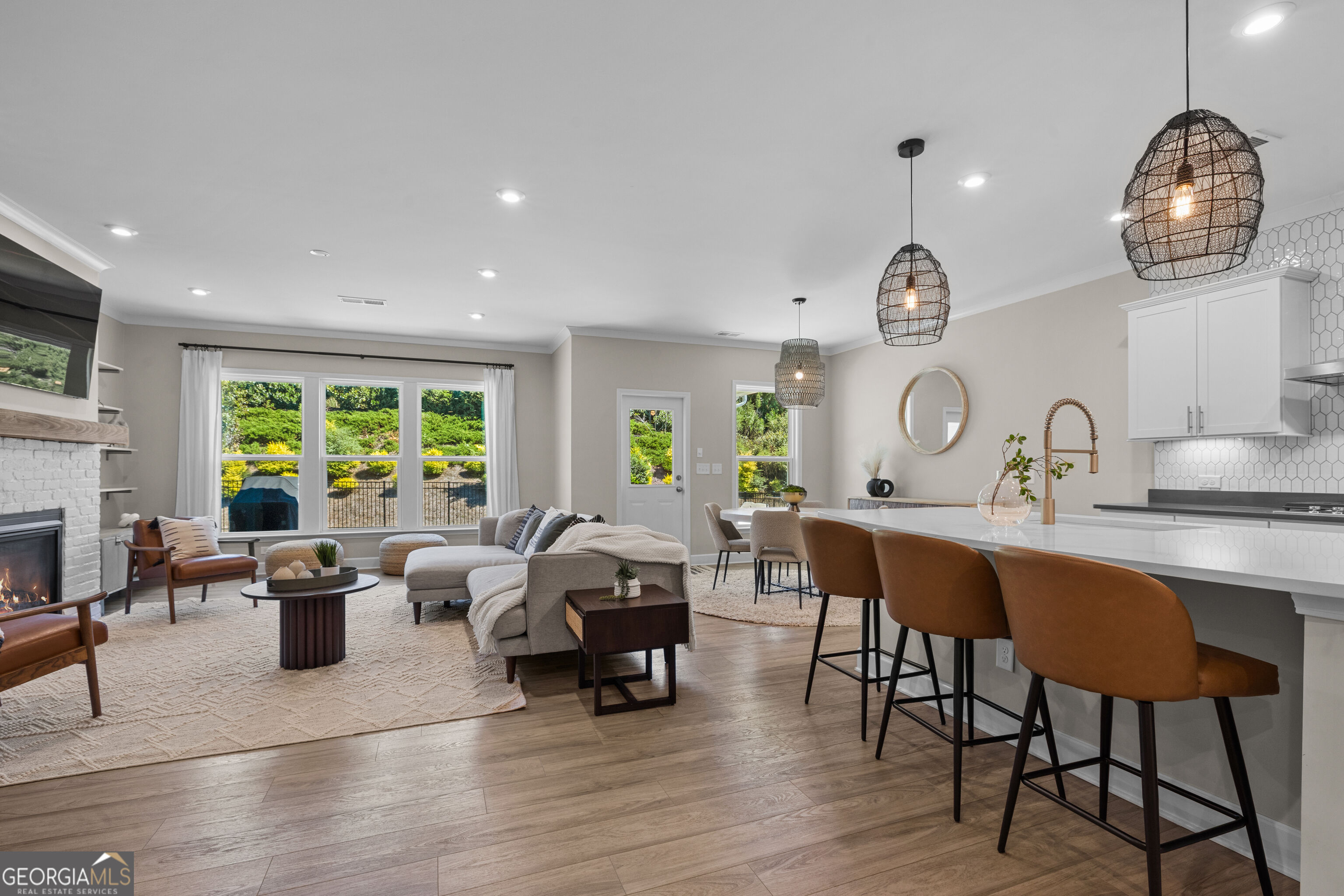 Open-plan living room and kitchen with a white island, brown stools, and a fireplace.