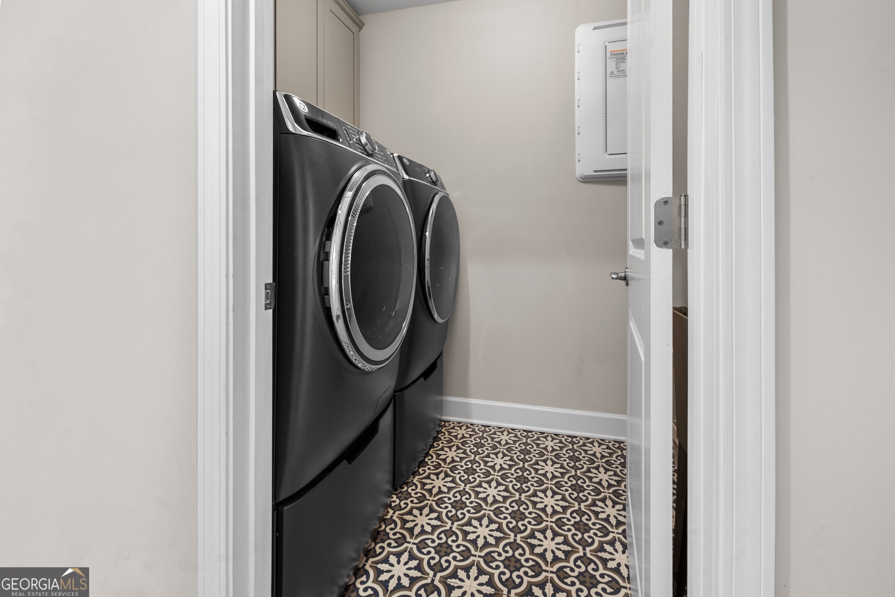 Laundry room with black front-loading washer and dryer and ornate patterned tile floor.