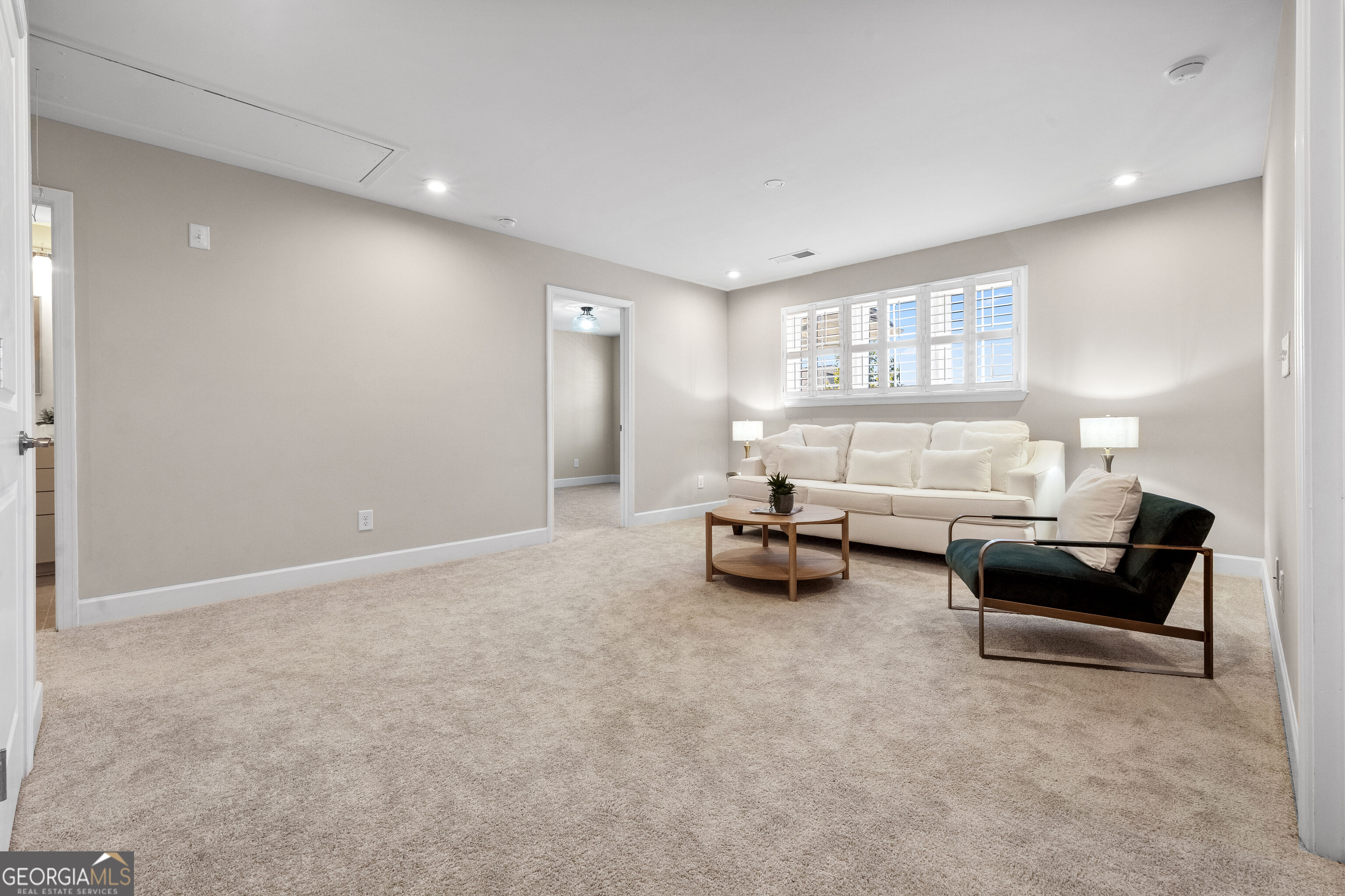 Living room with a white sofa beneath shuttered windows and a dark green accent chair.