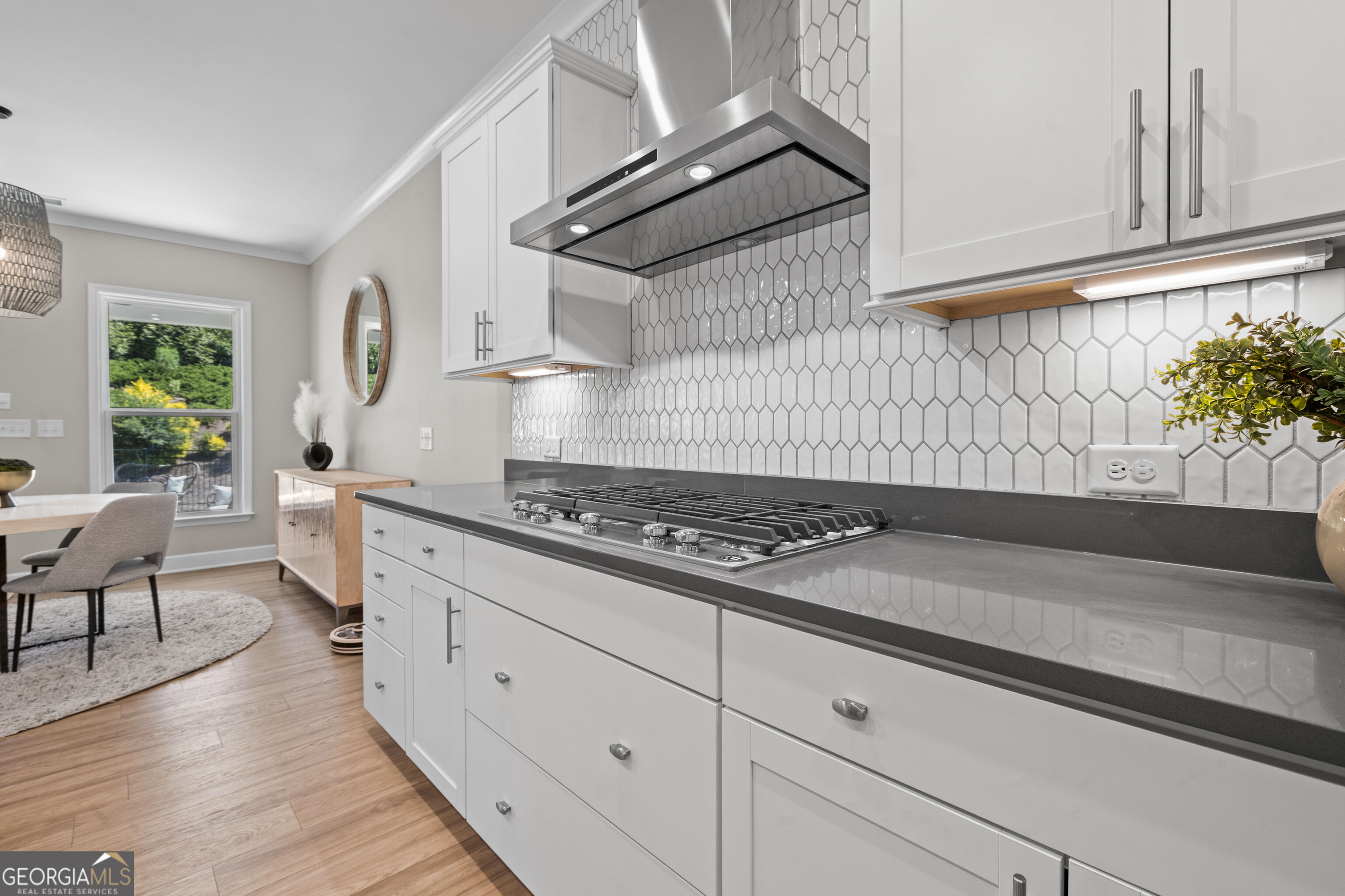Kitchen with white cabinets, geometric tile backsplash, and a stainless steel gas cooktop.