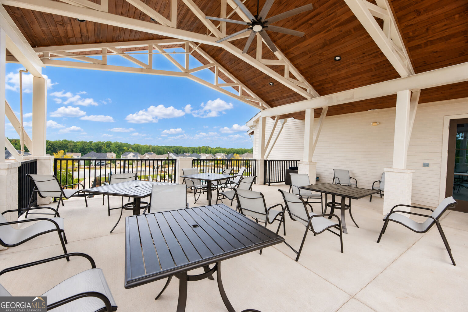 Covered patio with exposed white trusses, dining furniture, and views of nearby homes and trees.