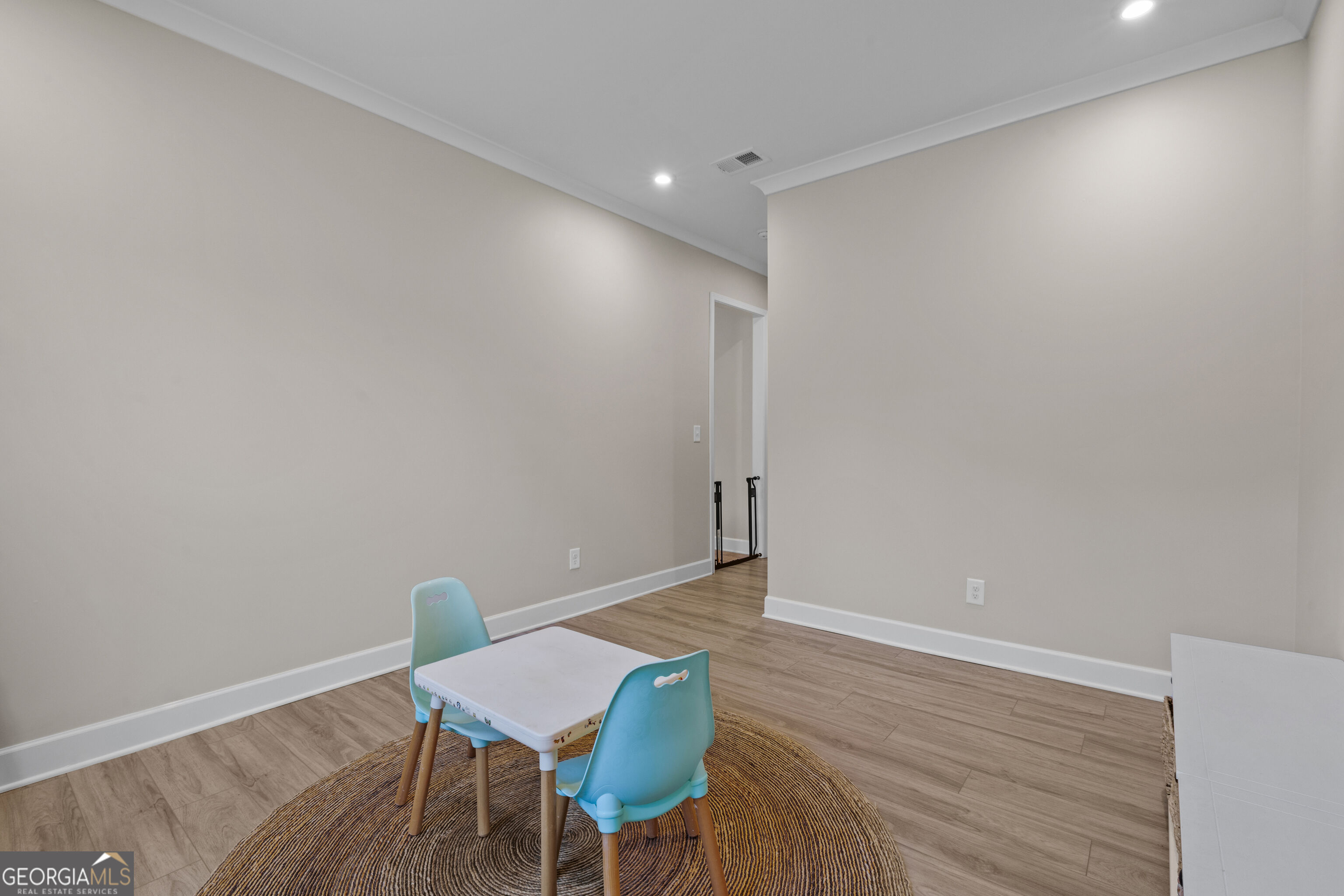 Room with wood-look floors and a small white table with turquoise chairs on a round rug.