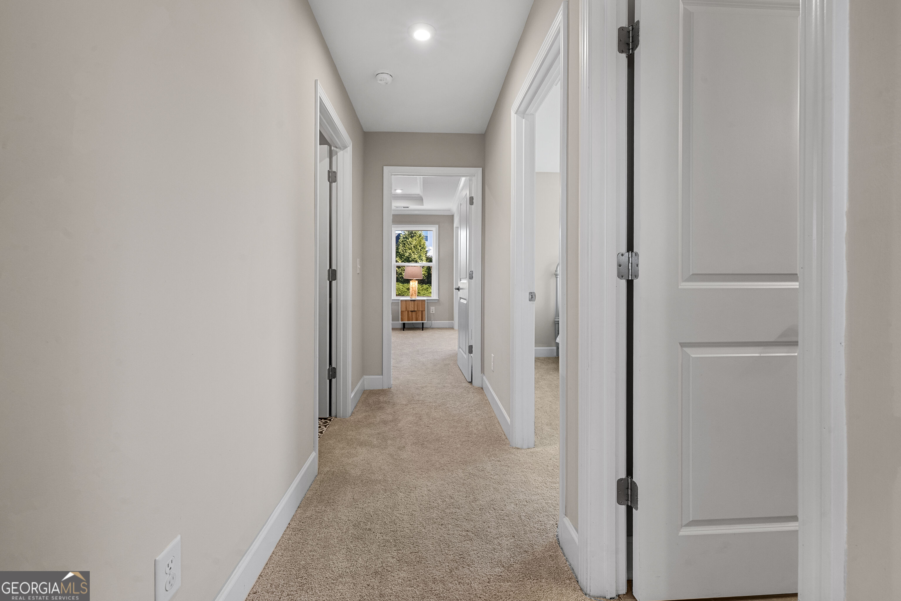 Carpeted hallway with open doorways and a wooden console table beneath a window.