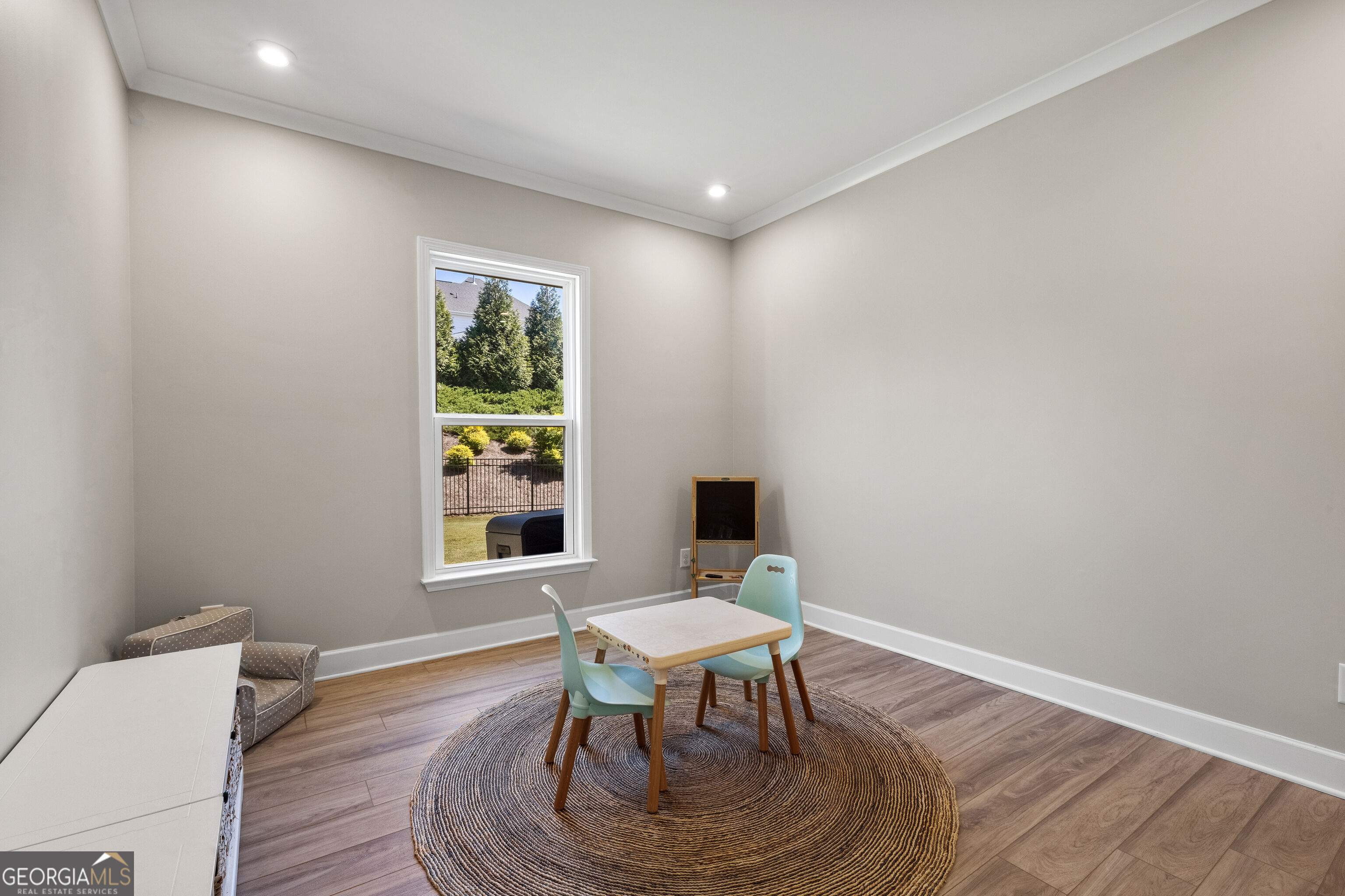 Playroom with a small table and mint chairs on a round woven rug beside a window.