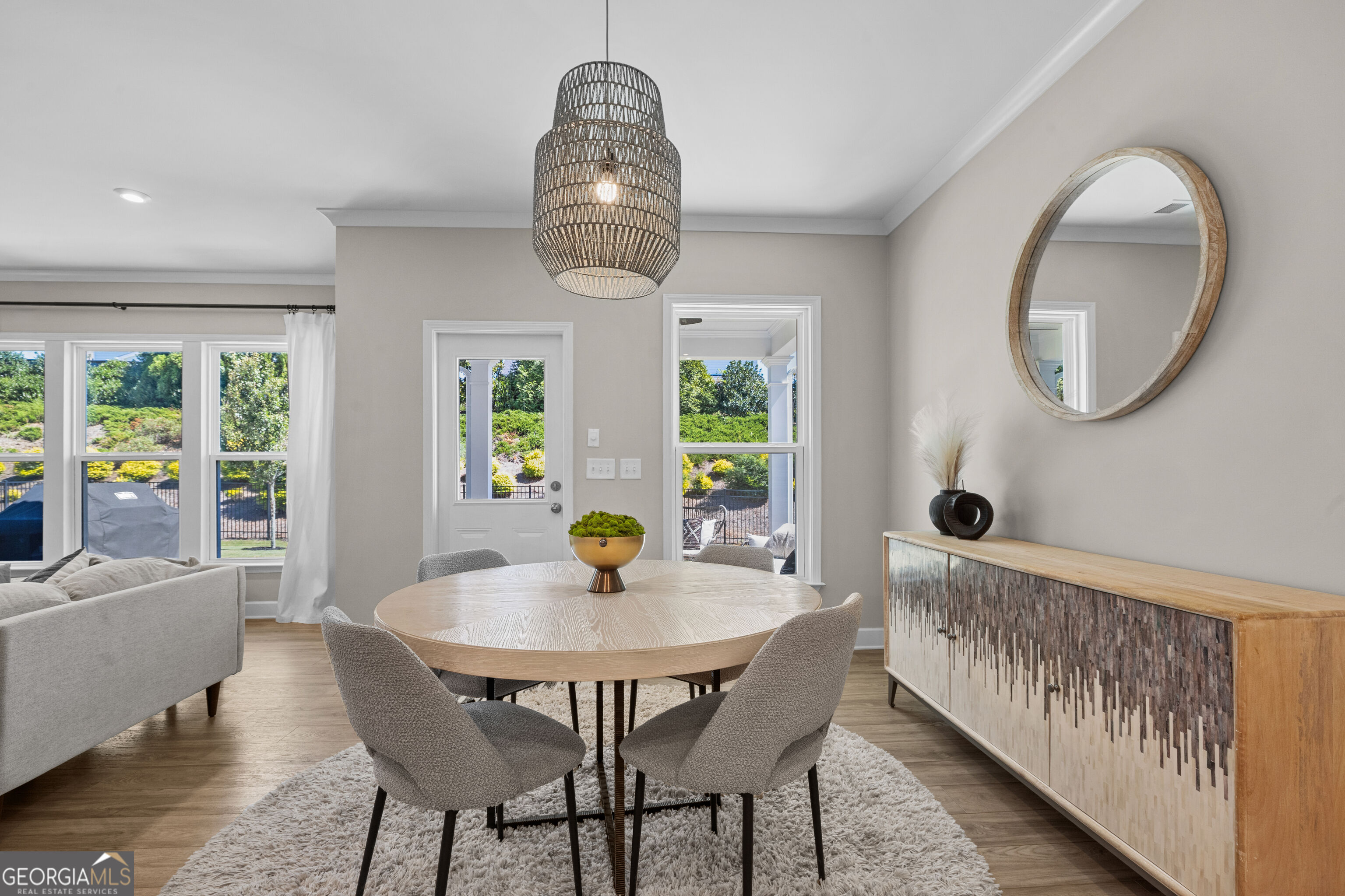 Dining area with a round wood table, woven pendant light, and windows overlooking a green yard.