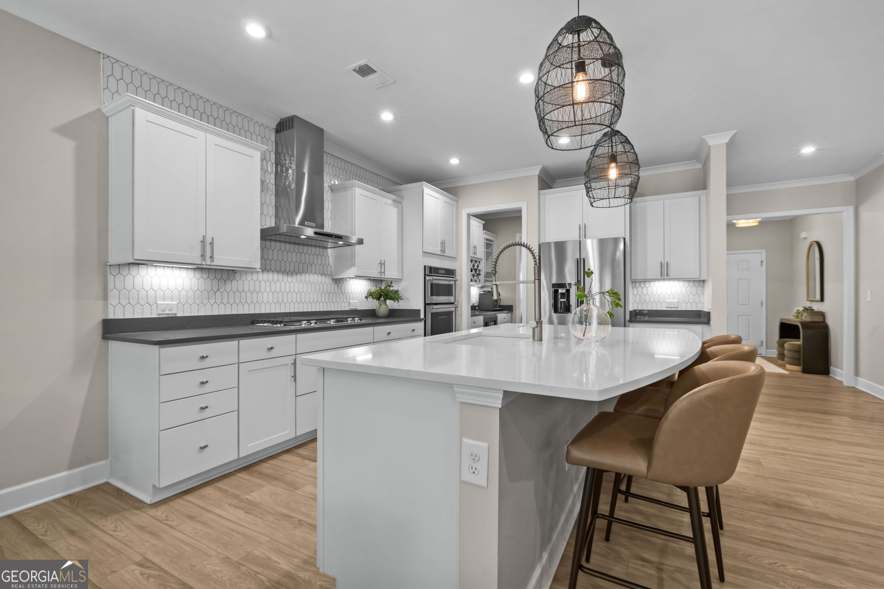 Modern kitchen with white cabinetry, a large island, tan bar stools, and stainless steel appliances.
