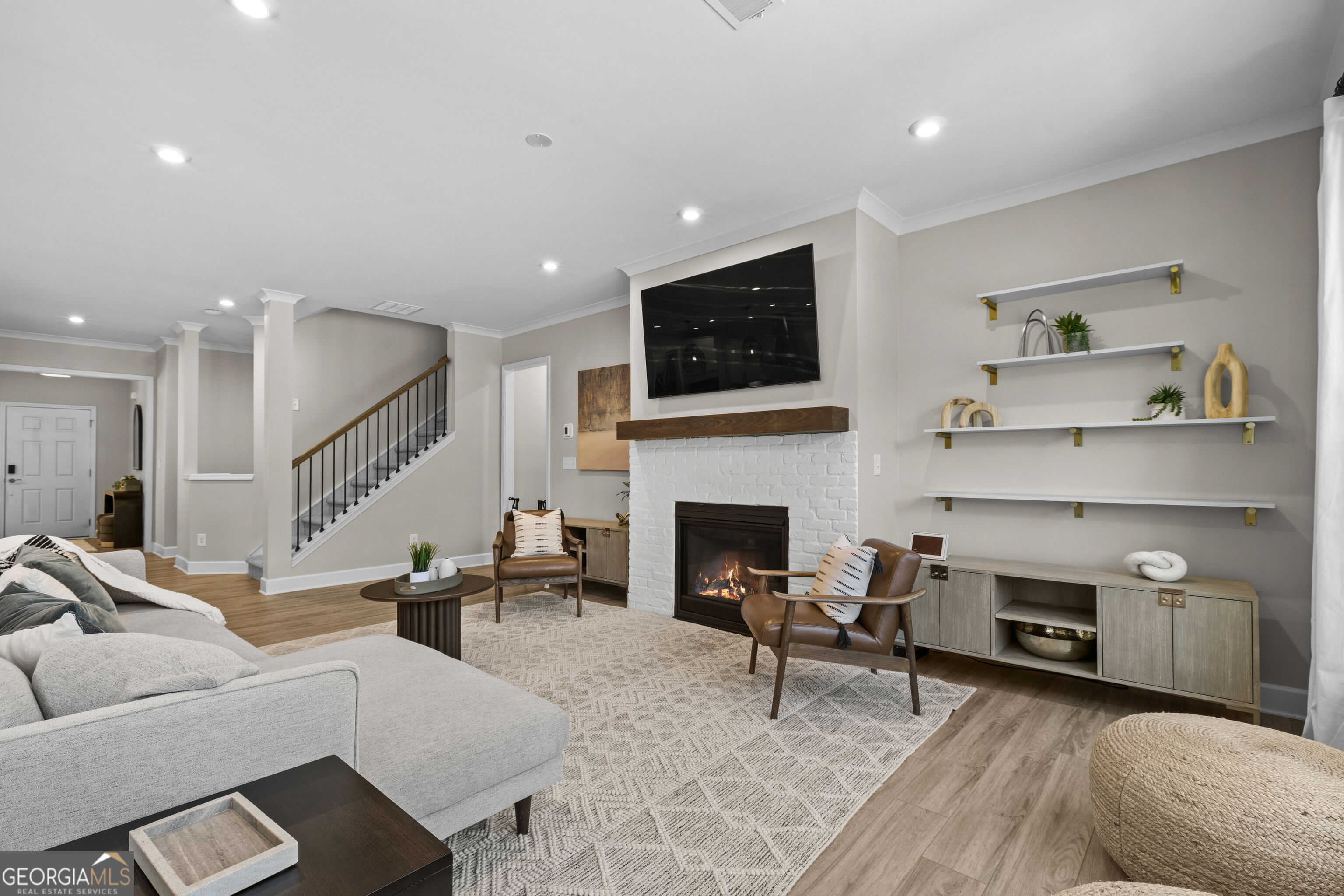 Living room with white brick fireplace, television, display shelves, and staircase.