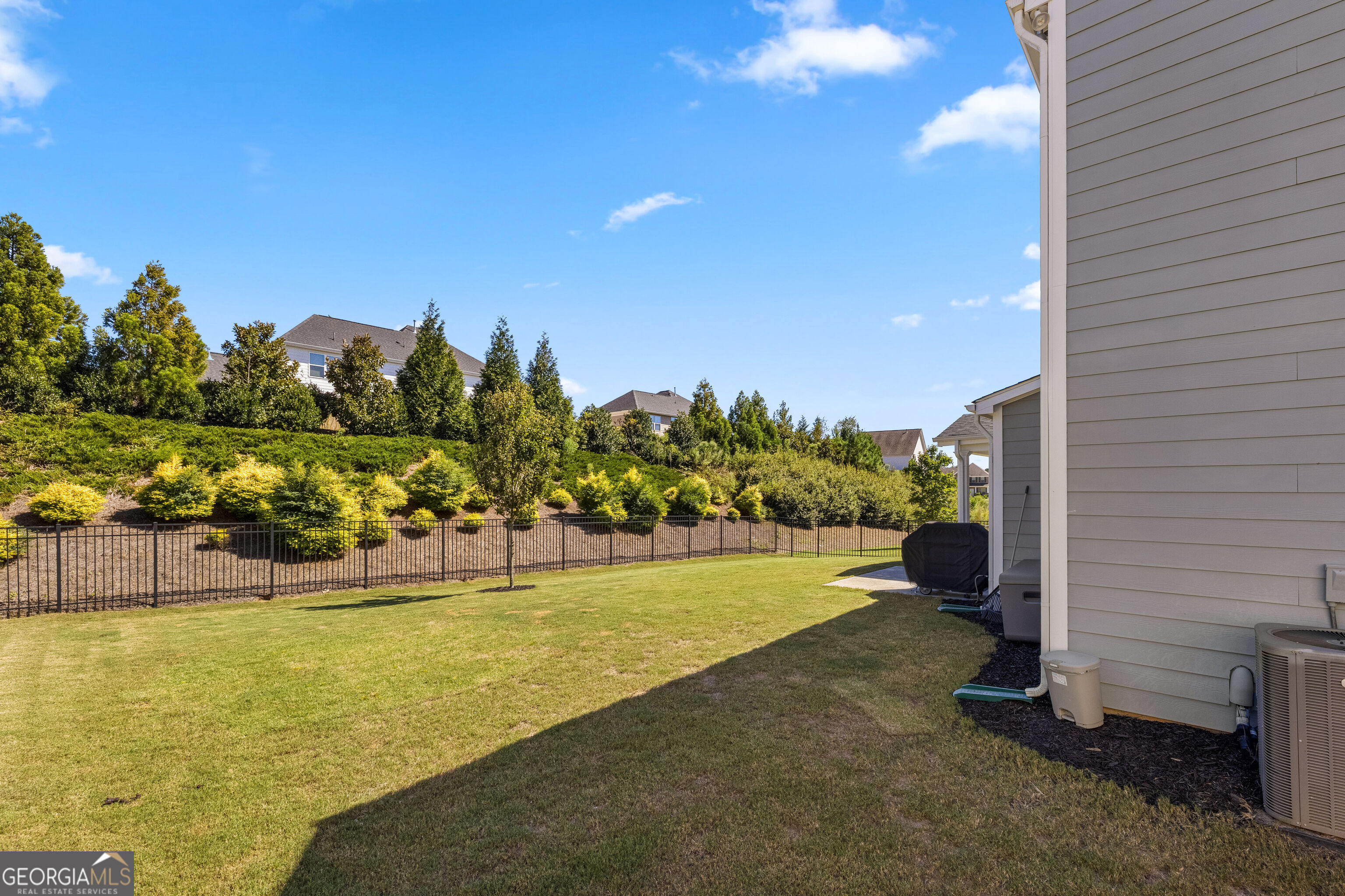Fenced backyard with a broad lawn, landscaped slope, and the home's gray-sided exterior.