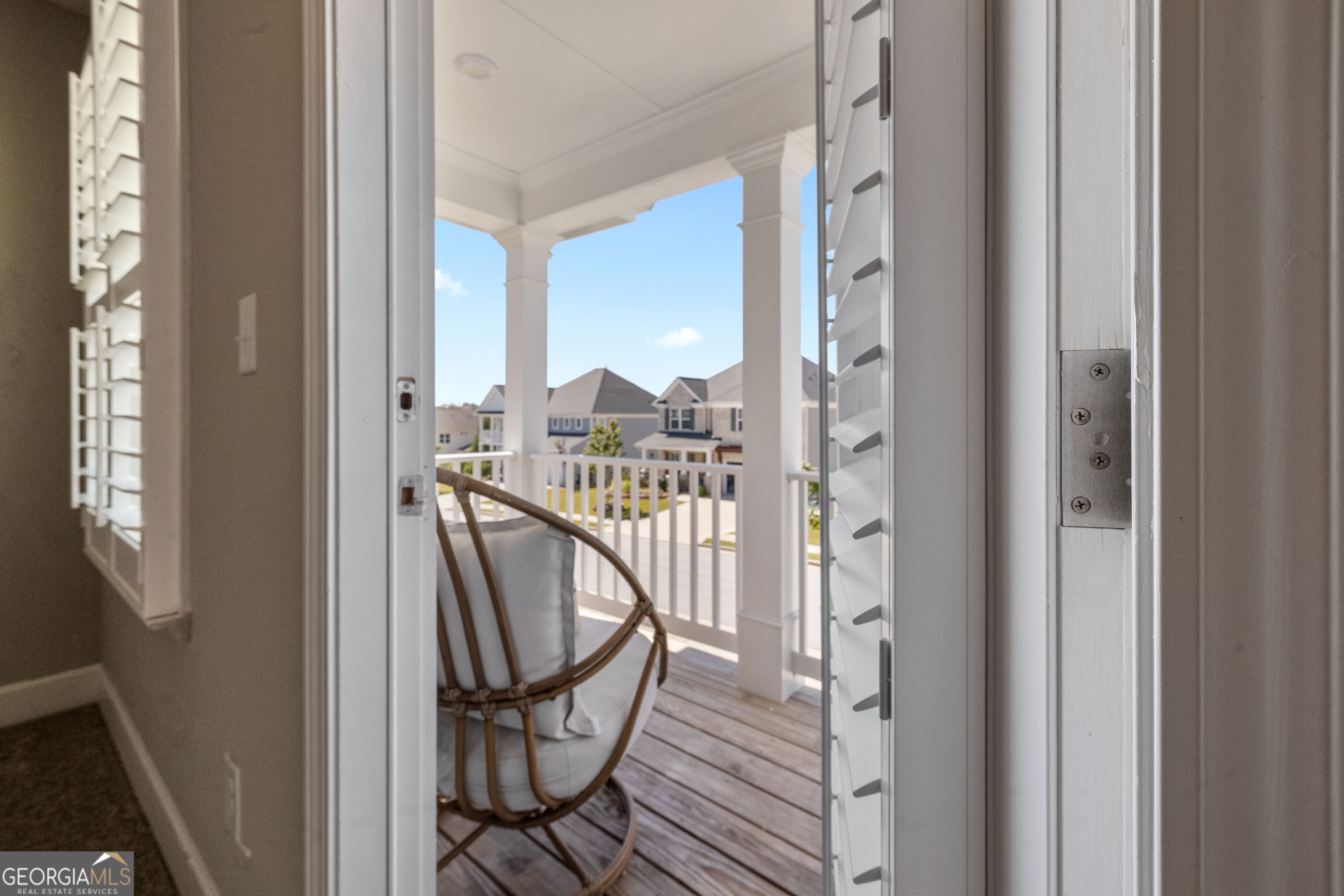 Covered porch with a hanging egg chair, white columns, and views of neighboring homes.