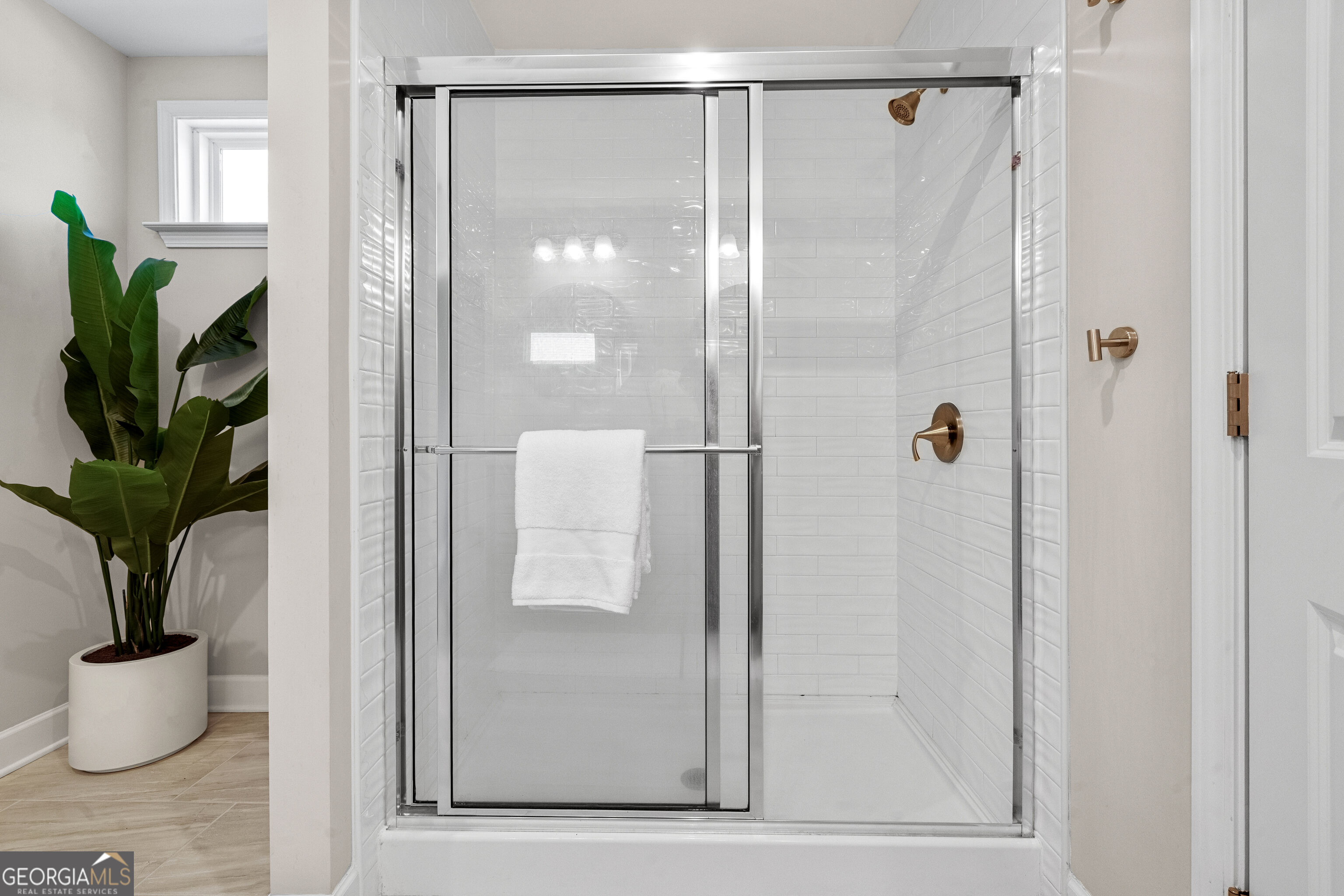 Glass-enclosed bathroom shower with white subway tile, bronze fixtures, and a potted tropical plant.