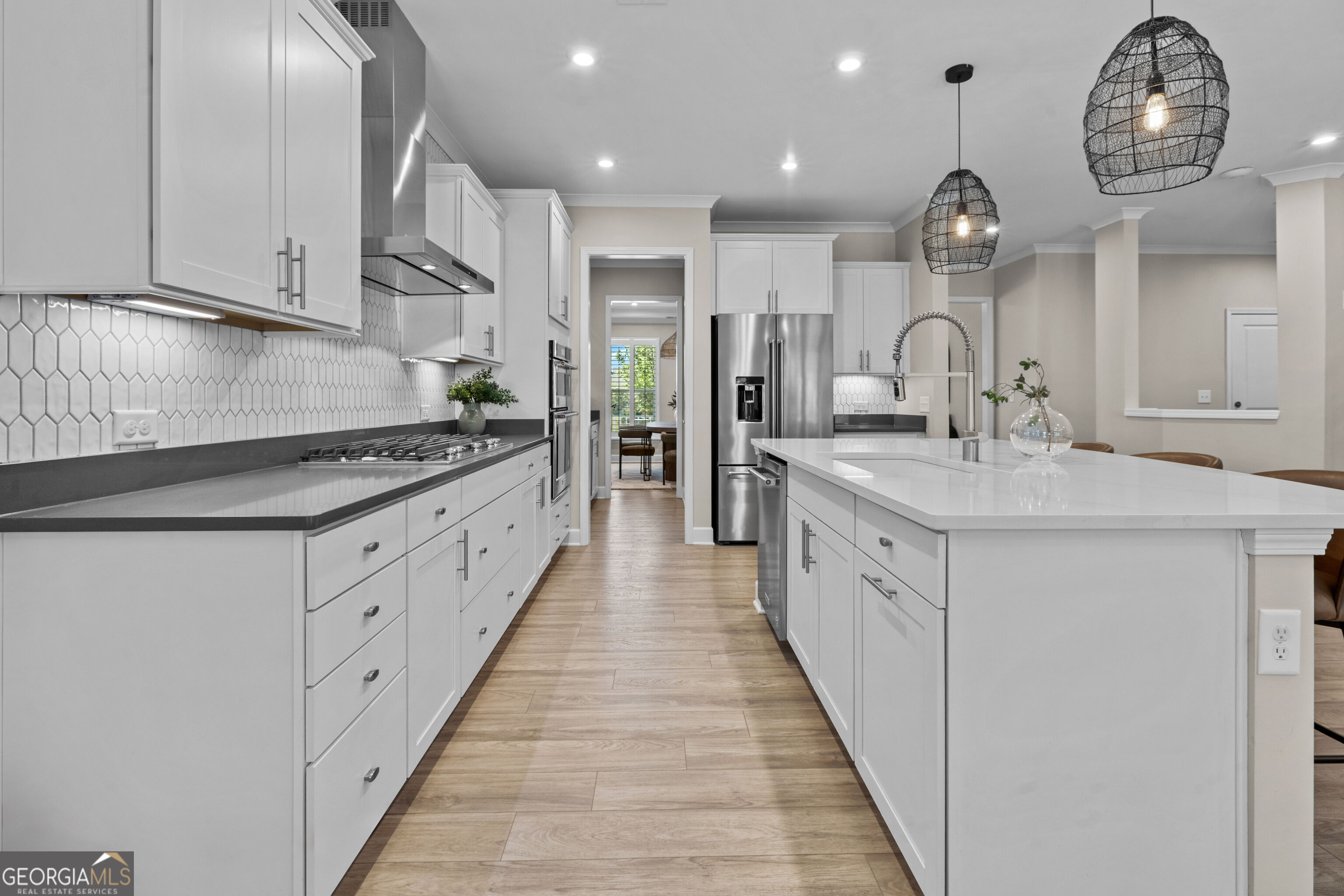 Bright kitchen with white cabinets, stainless steel appliances, and a large island beneath woven pendant lights.