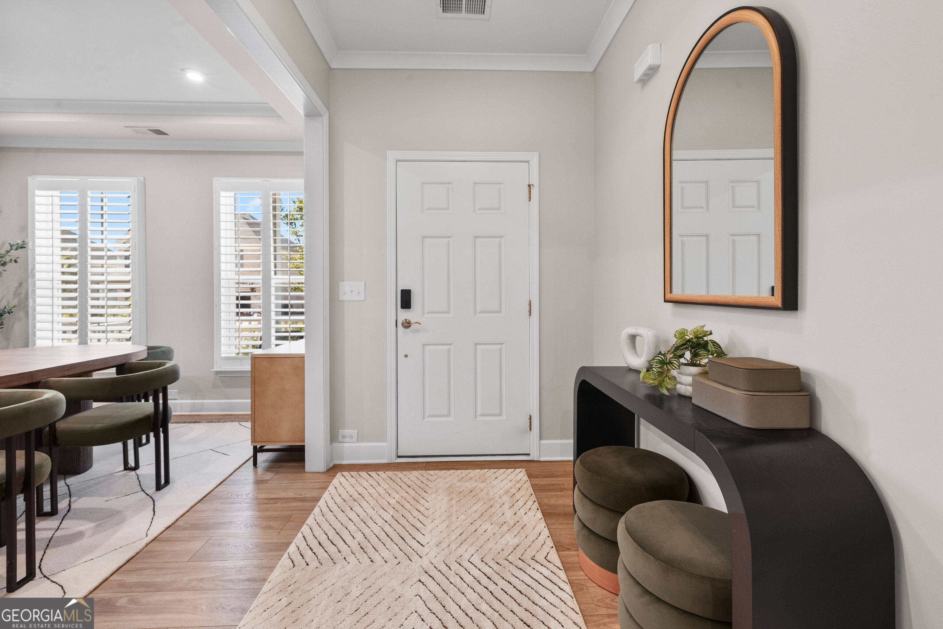 Furnished entryway with a white paneled door, arched mirror, black console, and view into the dining area.