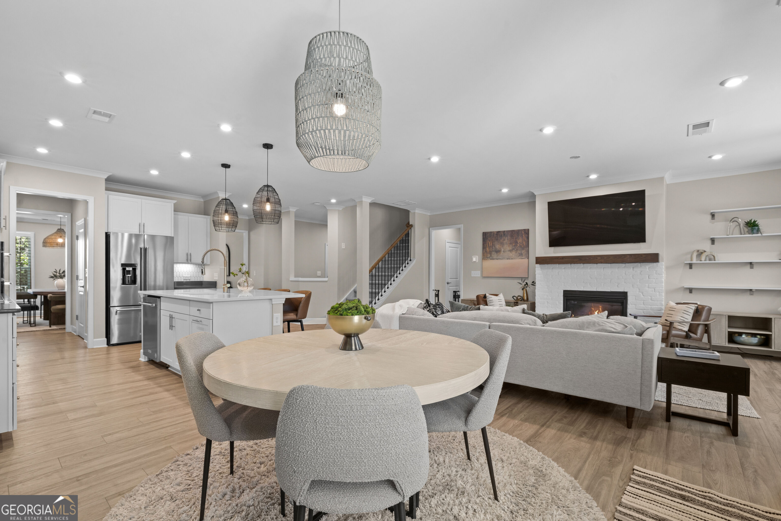 Open-concept dining and living room with a kitchen, white brick fireplace, and woven pendant lights.