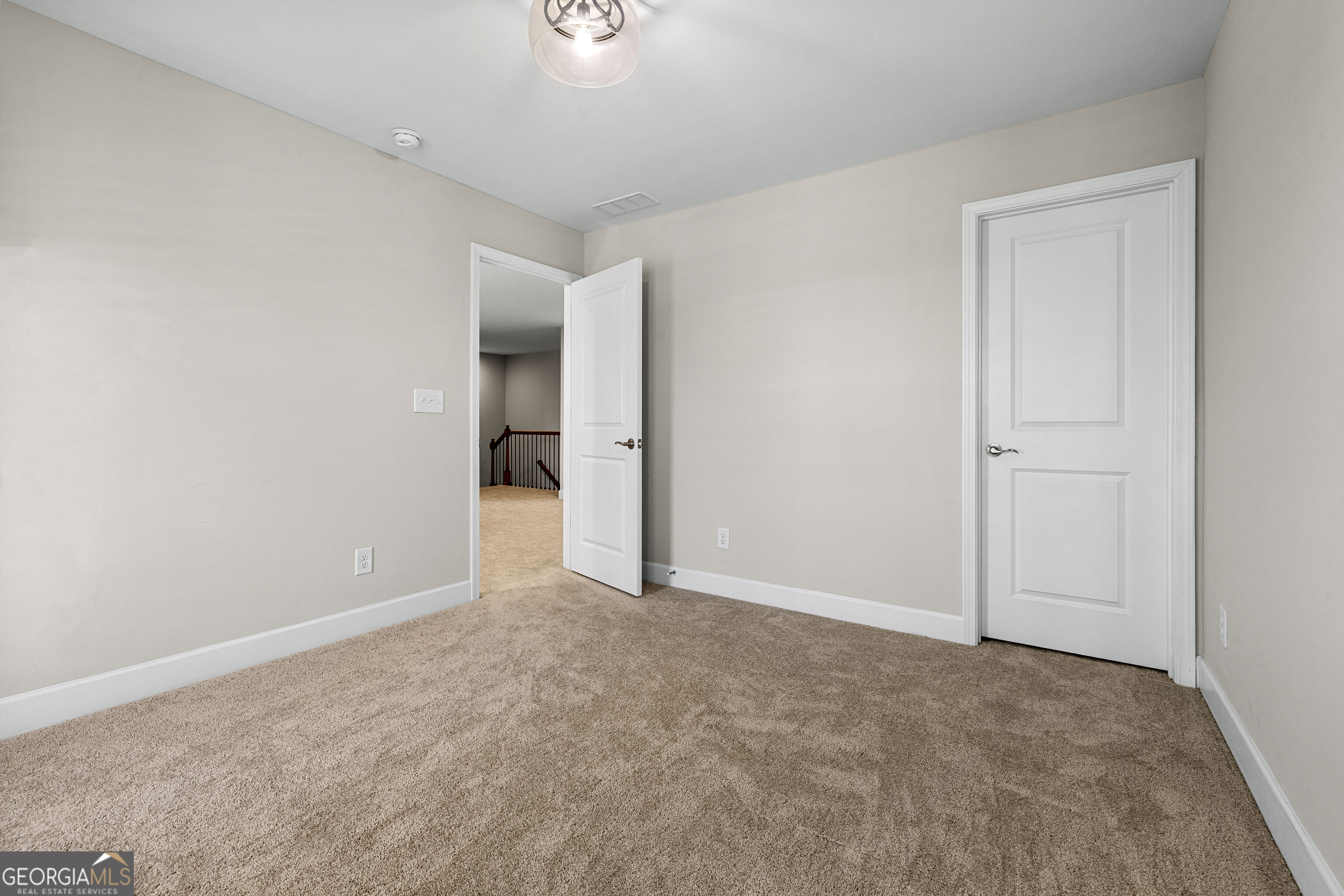 Empty carpeted room with neutral walls, a ceiling light, and an open door to a landing.