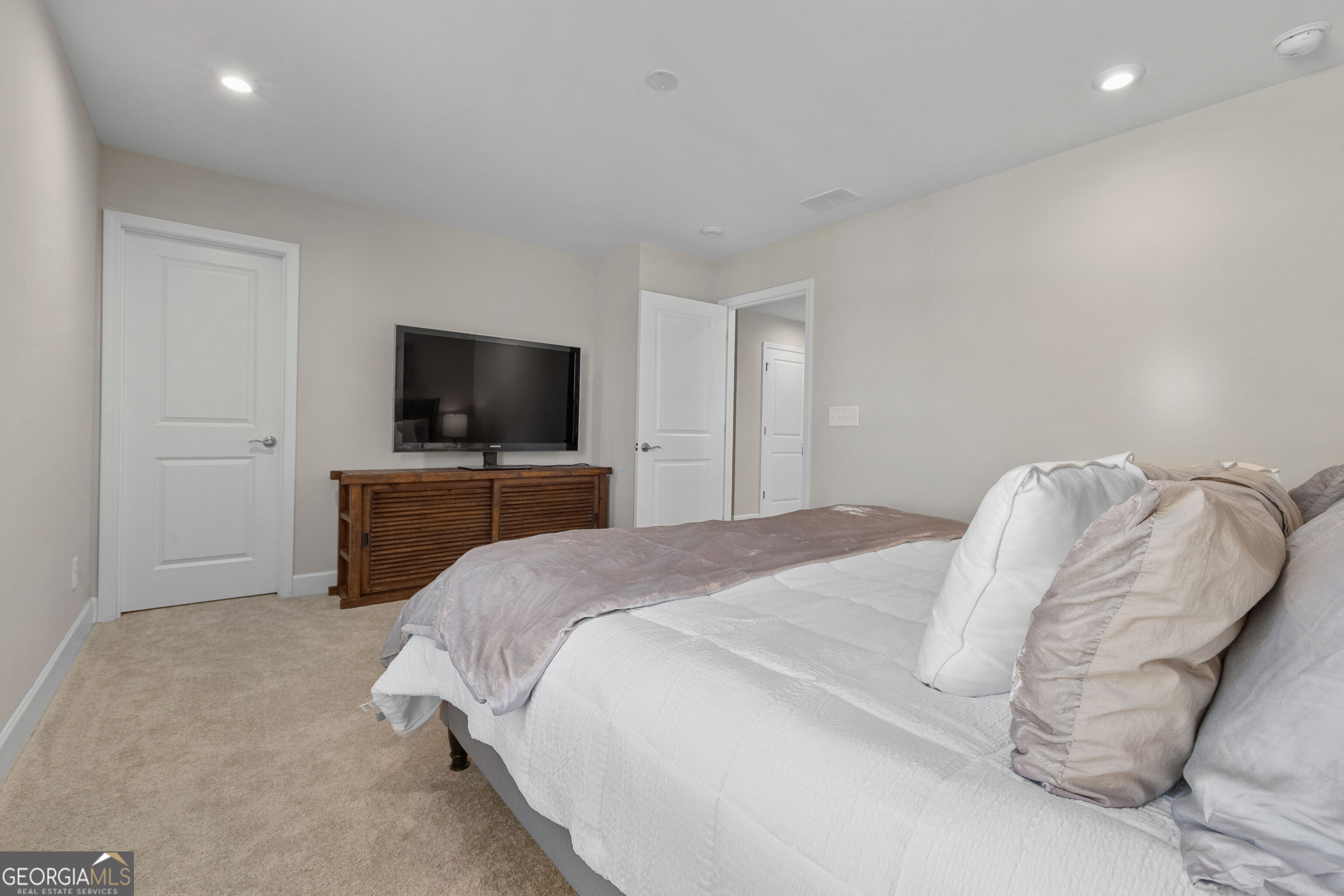 Bedroom with a large white-and-taupe bed and a television on a wooden console.
