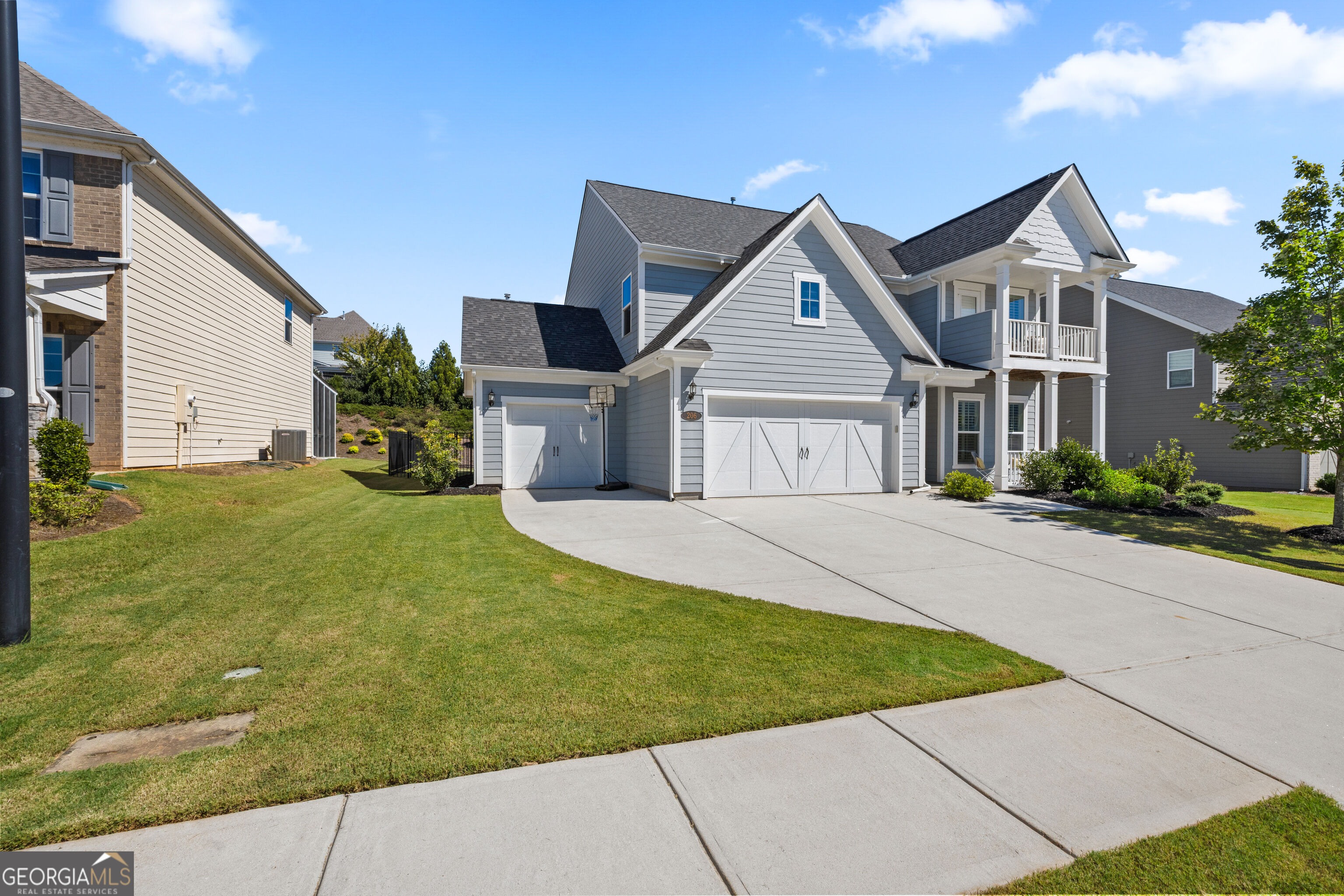Gray two-story house with a covered porch, upper balcony, double garage, and broad concrete driveway.