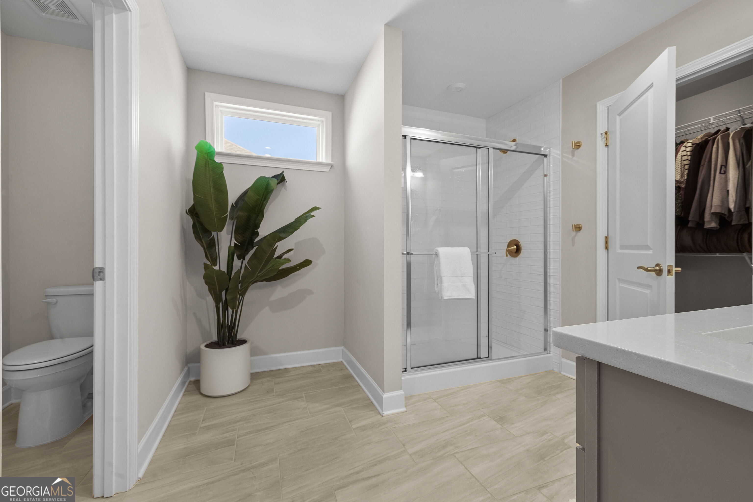 Bathroom with glass shower, large vanity, and a separate toilet area beside a narrow window.