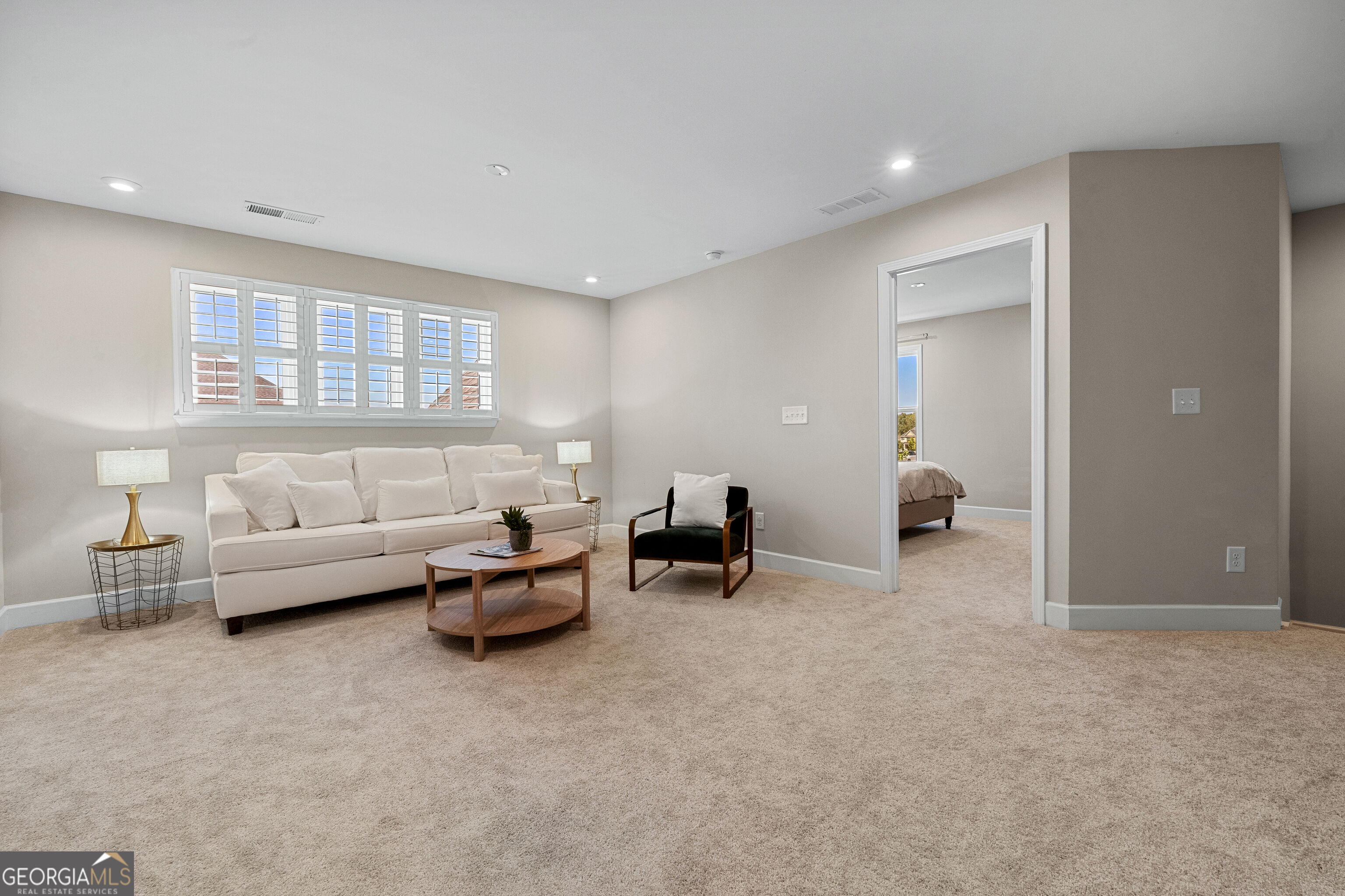 Furnished living area with plantation shutters, cream sofa, and doorway to a bedroom.