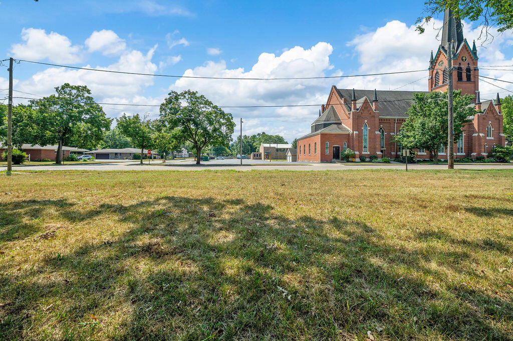 Grassy lot across from a red-brick church, with trees and utility wires along the street.