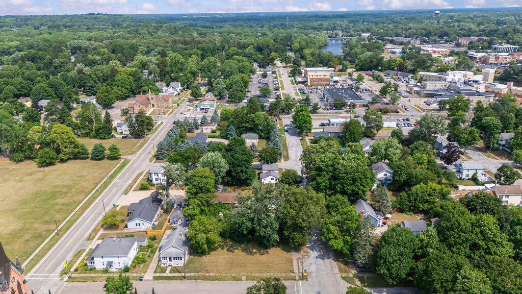 Aerial view of a tree-lined town center with homes, shops, and a river in the distance.