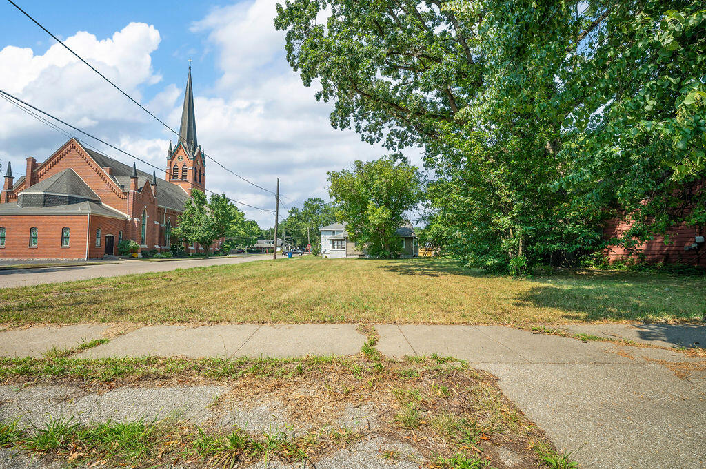 Vacant grassy lot beside a sidewalk, with a red-brick church across the street.