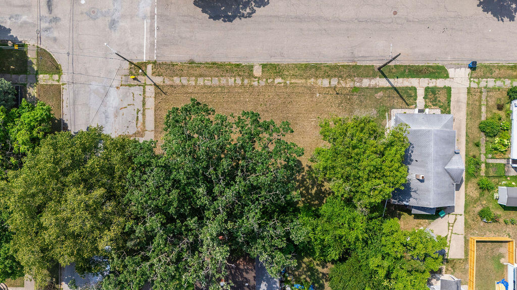 Aerial view of a house and lawn, partly shaded by mature trees beside the street.