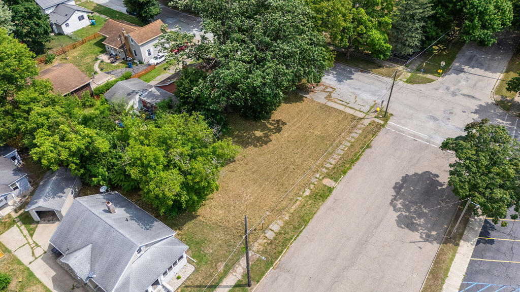 Aerial view of a vacant, tree-bordered lot beside a street intersection.