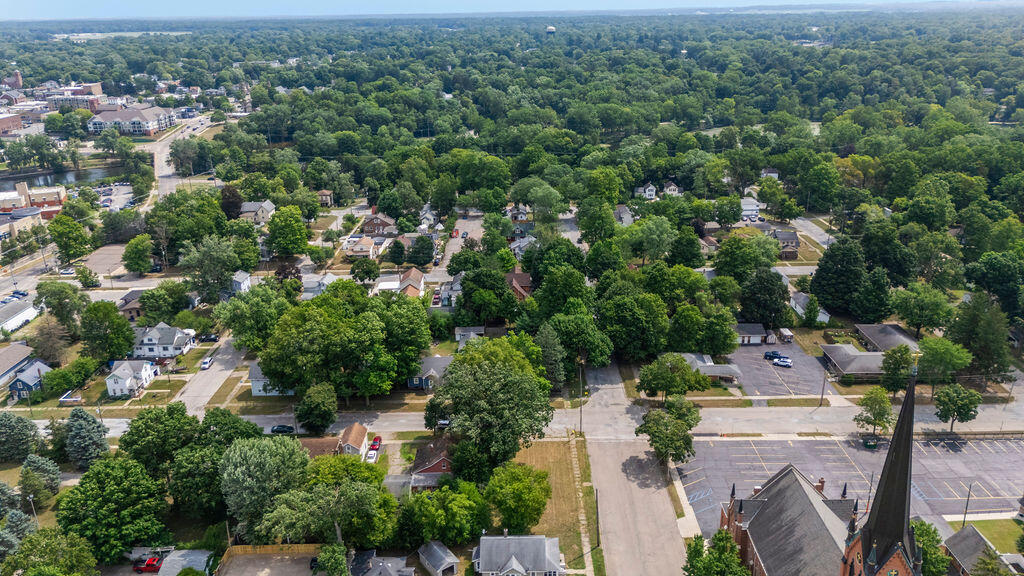 Aerial view over a leafy neighborhood and downtown streets, with a church steeple in the foreground.