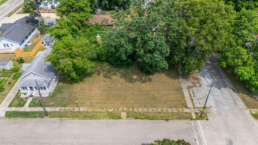 Vacant corner lot with a grassy yard, mature trees, and neighboring homes.