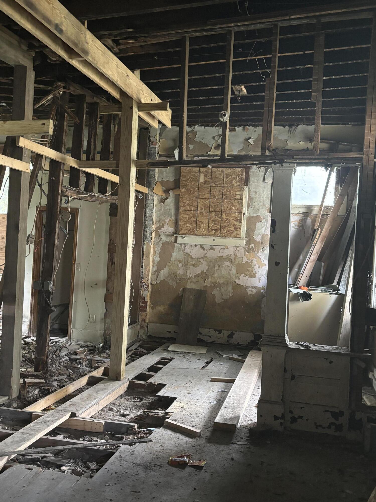 Gutted interior with exposed framing, damaged plaster walls, and sections of flooring removed.