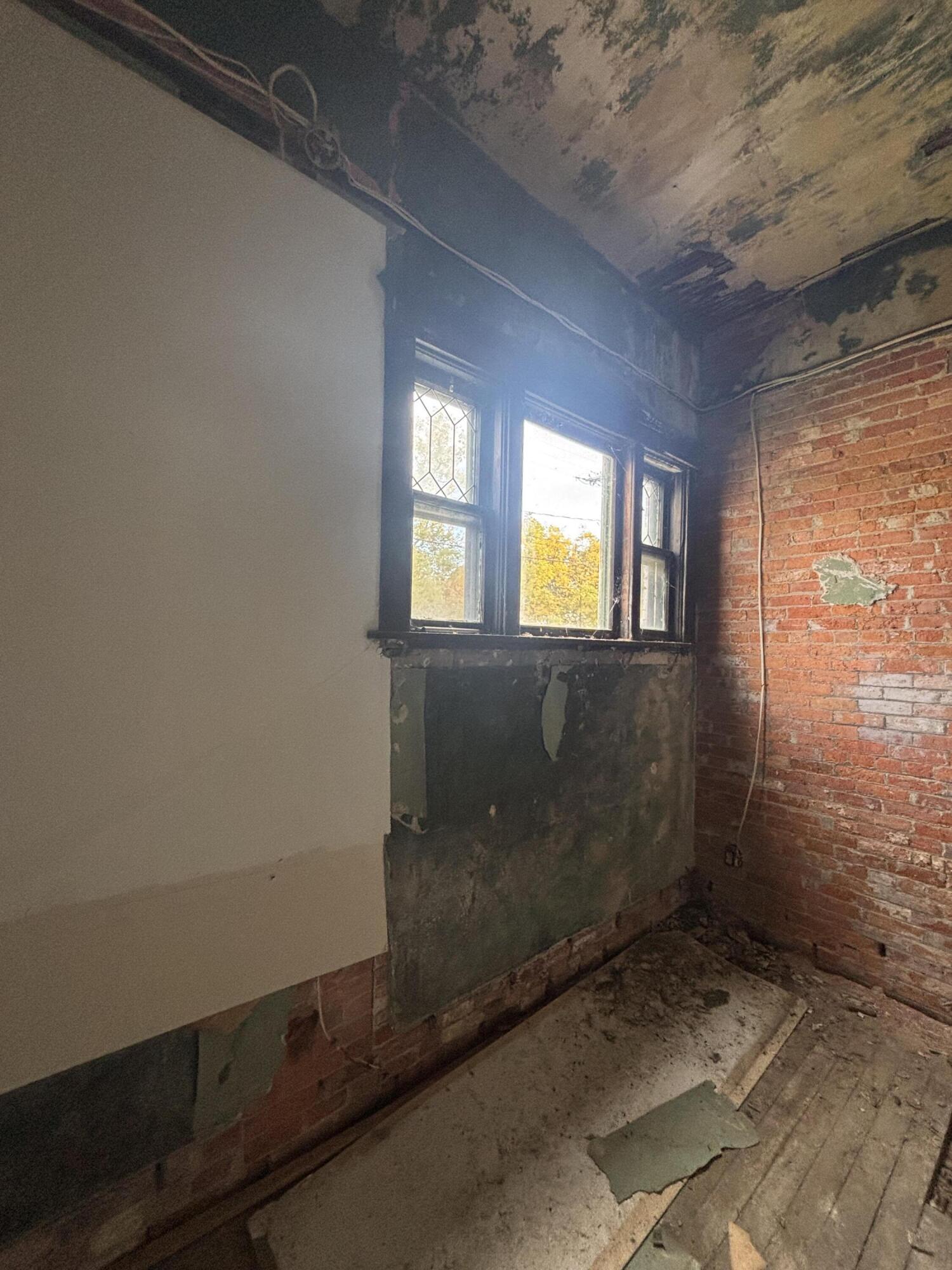 Unfinished room with exposed brick walls, peeling ceiling, and tall leaded windows.