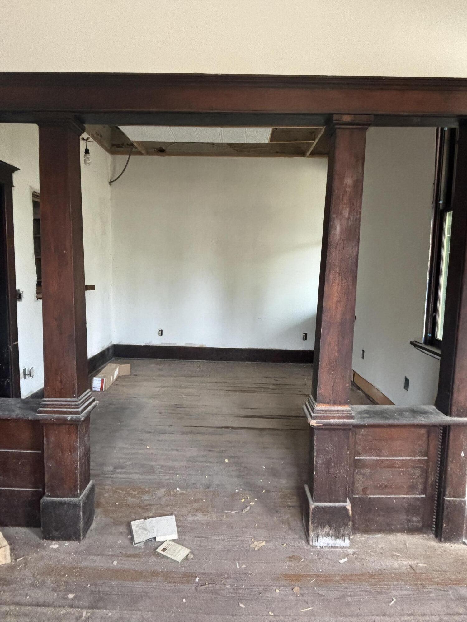 Unfinished room with dark wood columns, worn plank flooring, and an open ceiling section.
