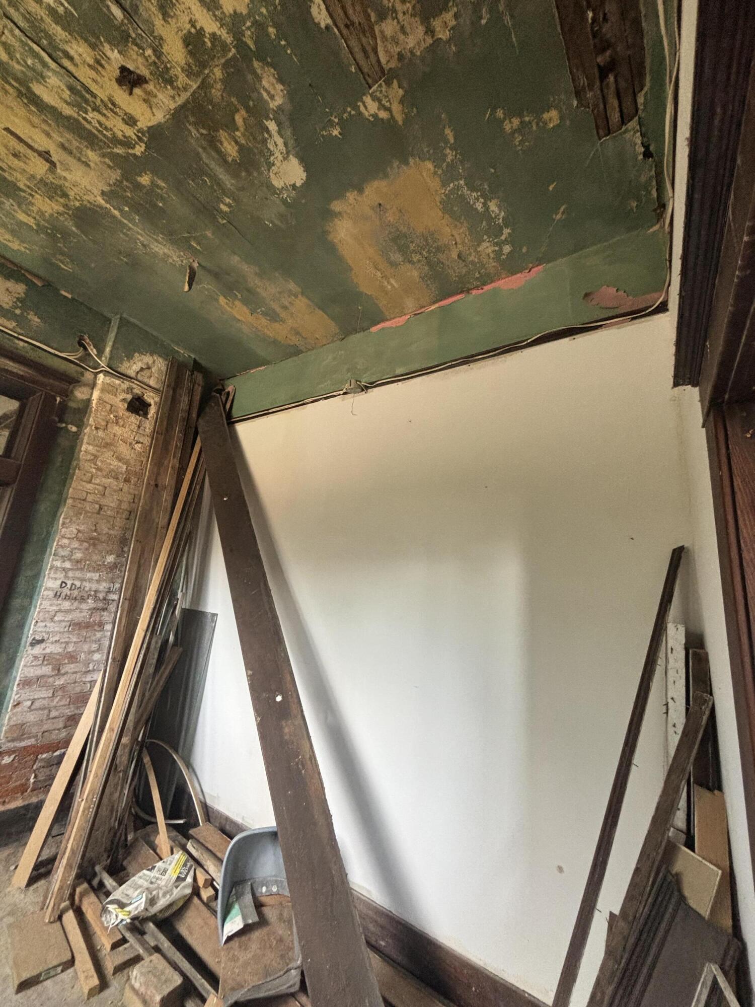Renovation interior with peeling green ceiling, exposed brick, and a diagonal wooden support.