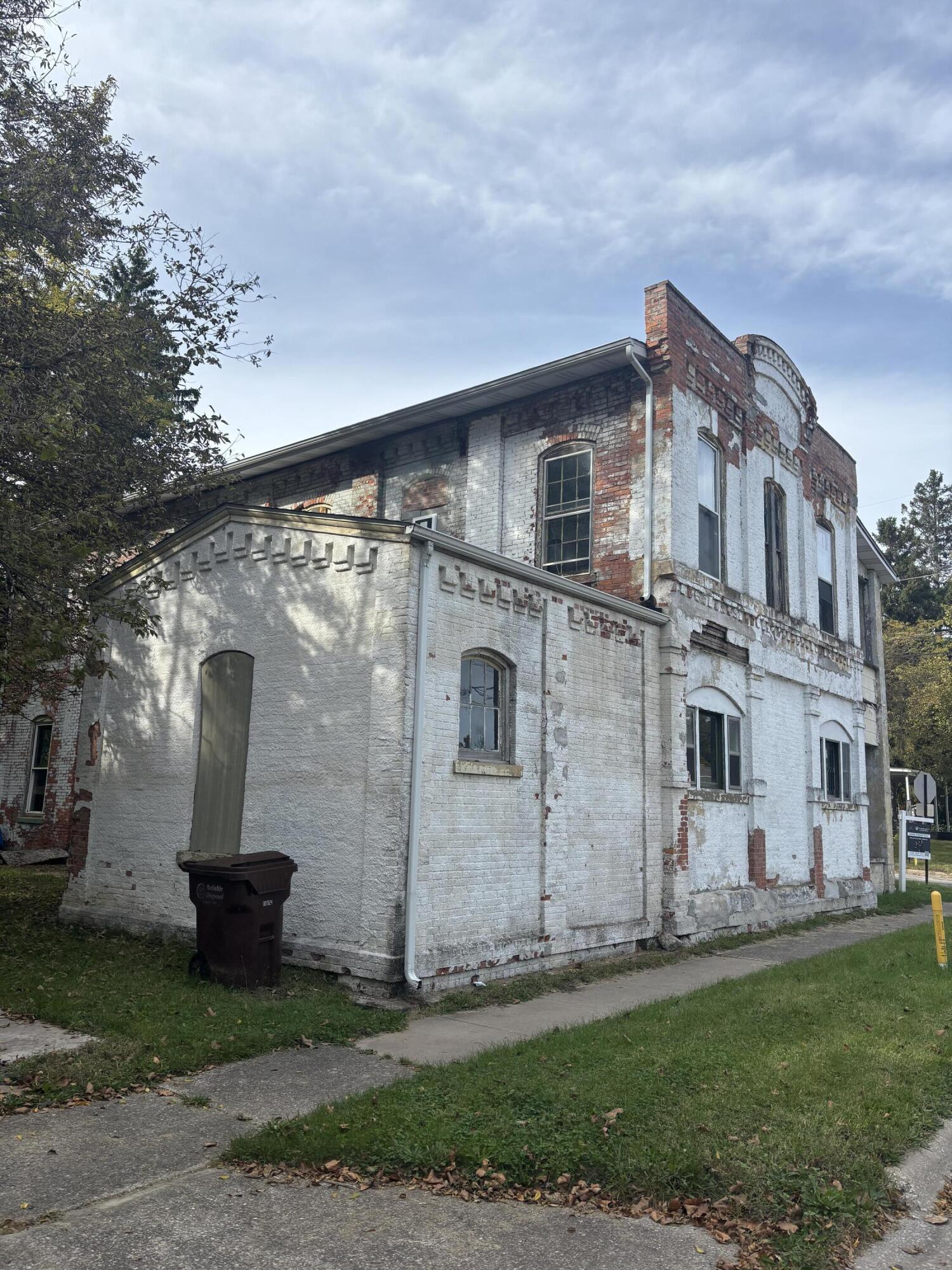 Weathered two-story brick building with a white facade, exposed red brick, and tall arched windows.