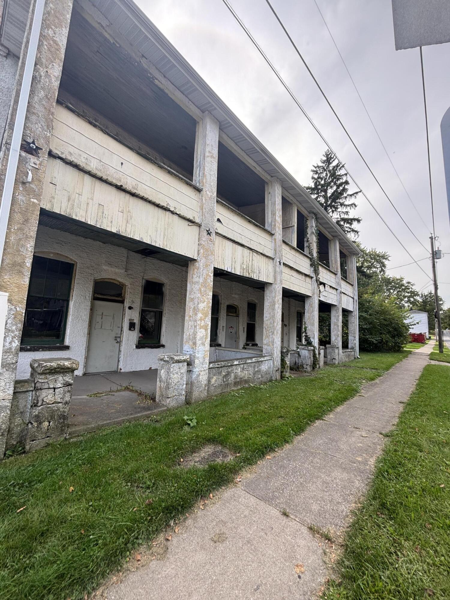 Weathered two-story building with a long covered porch beside a sidewalk.