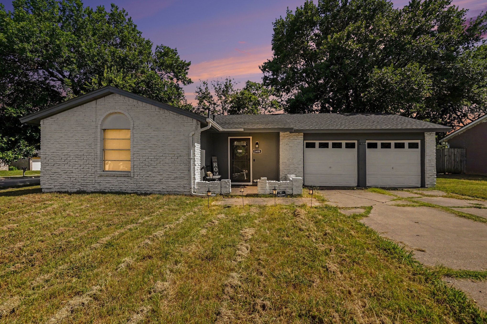 Single-story white-brick home with a covered entry and two-car garage at dusk.