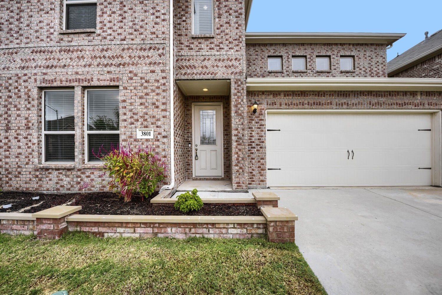 Two-story brick home with a recessed entry, white double garage door, and landscaped front bed.