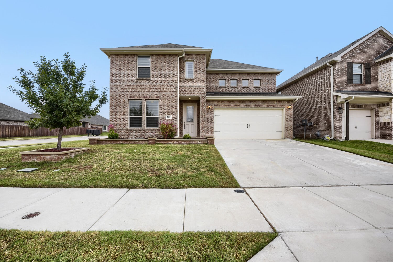 Two-story brick house with a white garage door, front lawn, and driveway.