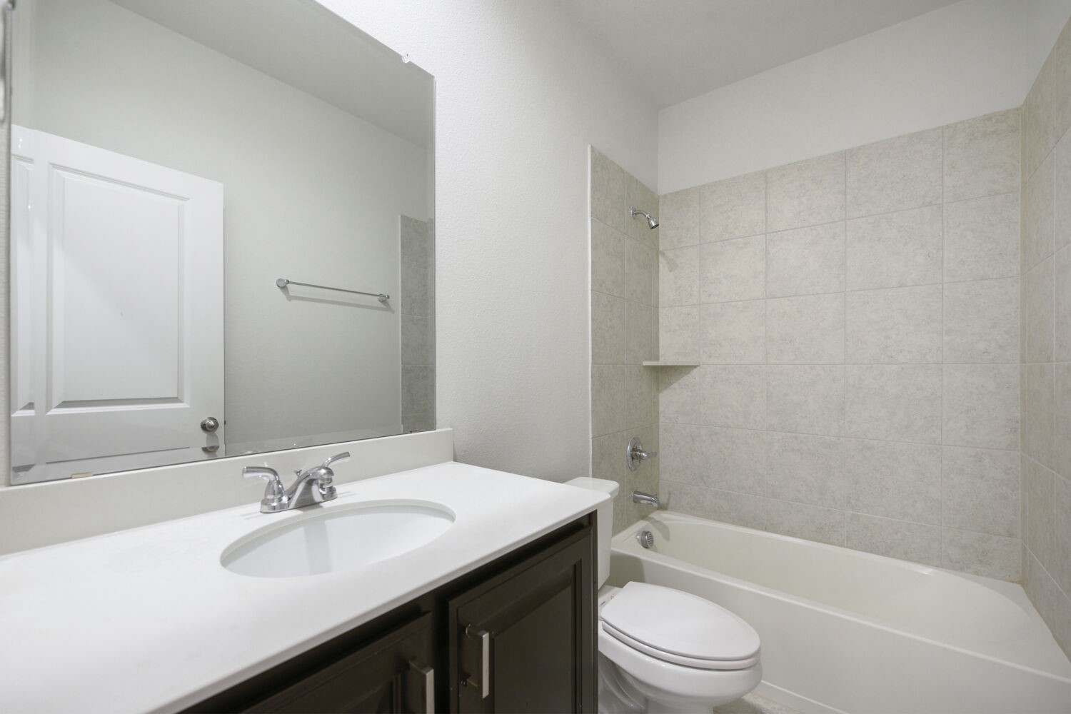 Bathroom with a dark vanity, large mirror, toilet, and tiled tub-shower.