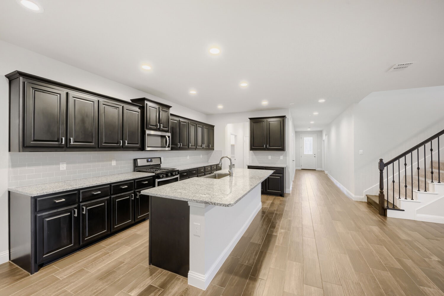 Kitchen with dark cabinets, a granite island, and a staircase beside the hallway.