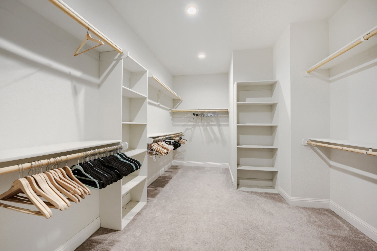 Walk-in closet with built-in shelving, hanging rods, and carpeted floor.