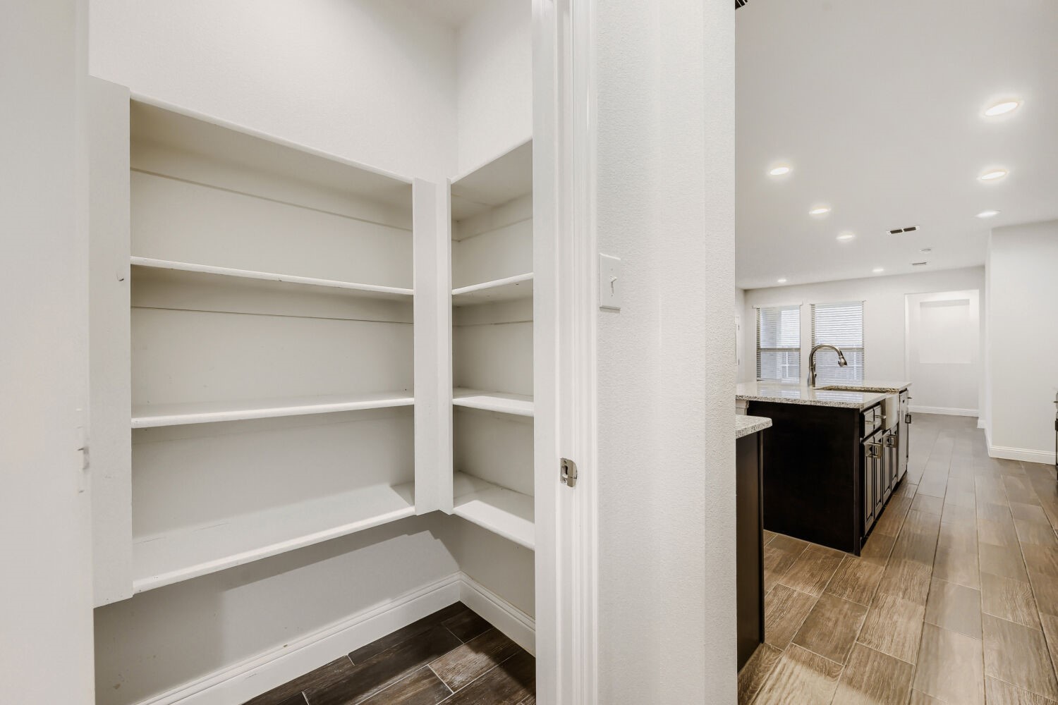 Walk-in pantry with open white shelves beside a kitchen island.