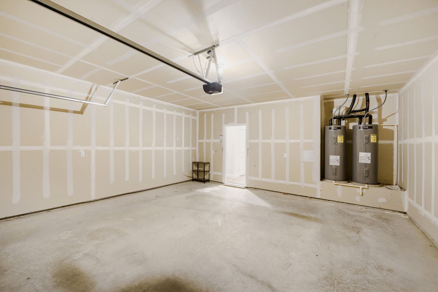 Unfinished garage with a concrete floor, garage door opener, and two water heaters.