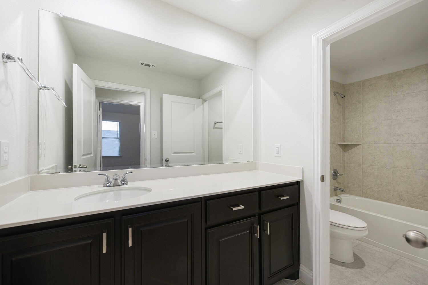 Bathroom with a dark vanity, wide mirror, and tiled tub-shower.