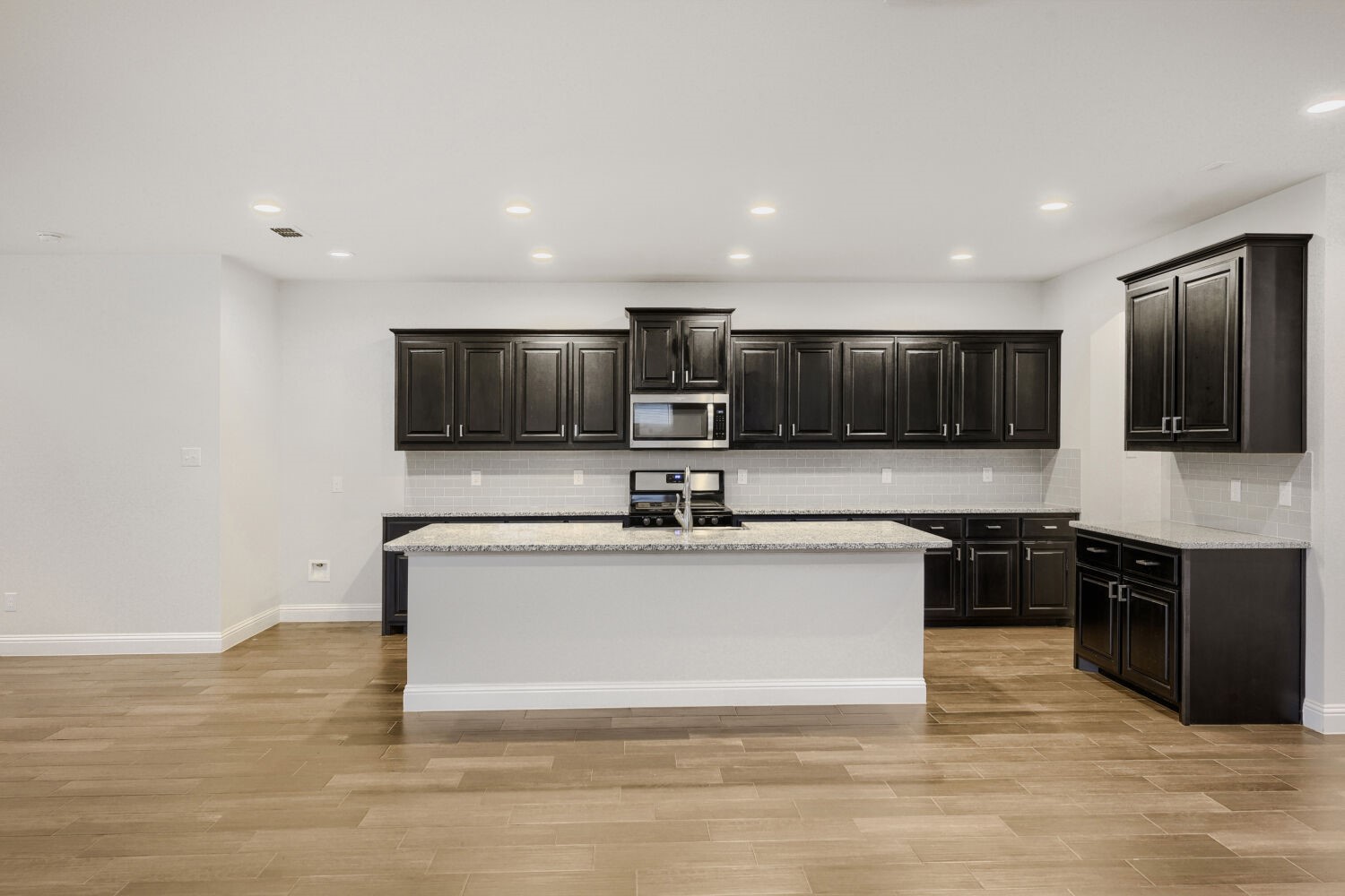 Kitchen with dark wood cabinets, a large island, and wood-look tile flooring.