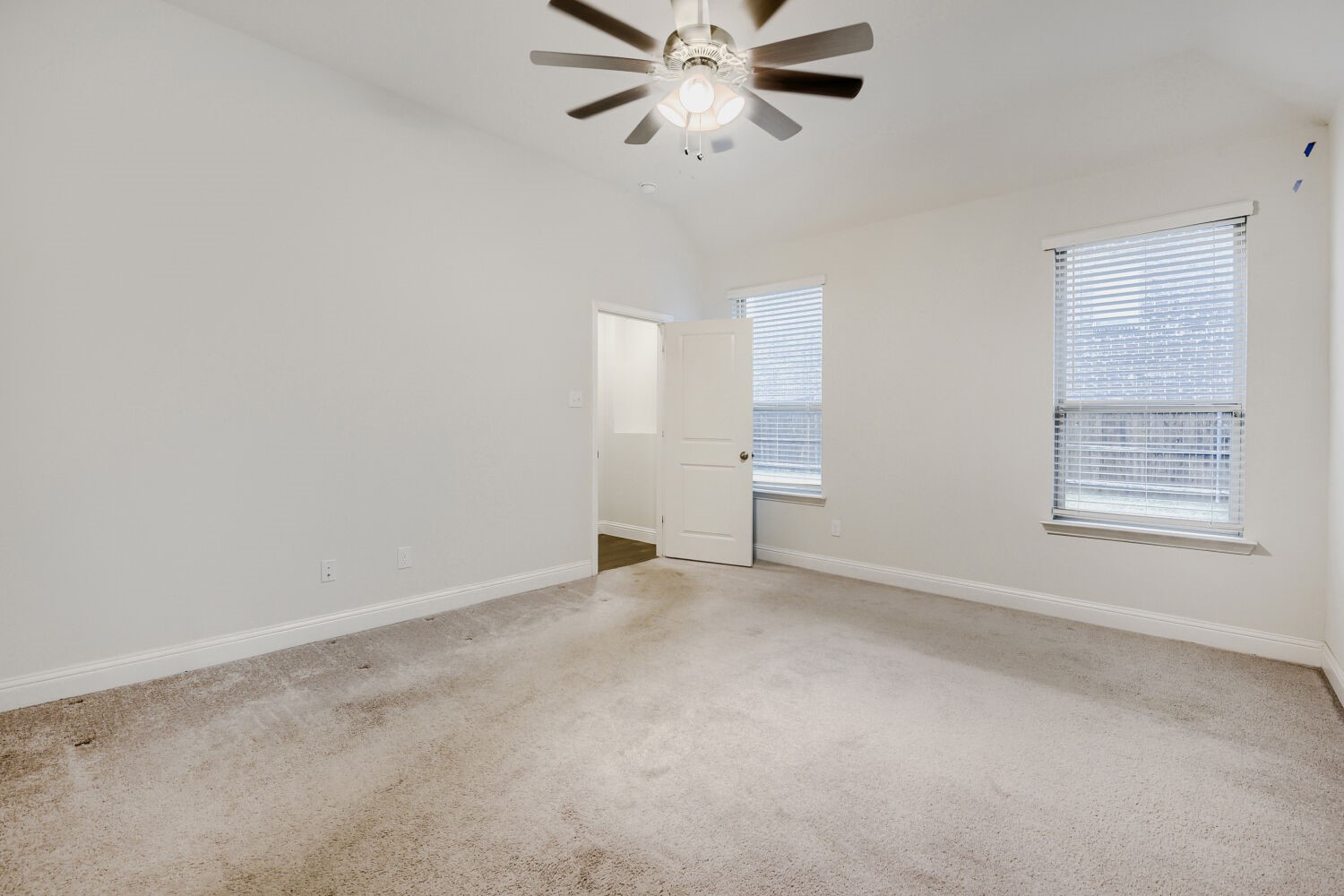 Empty carpeted bedroom with two windows, an open door, and a ceiling fan.