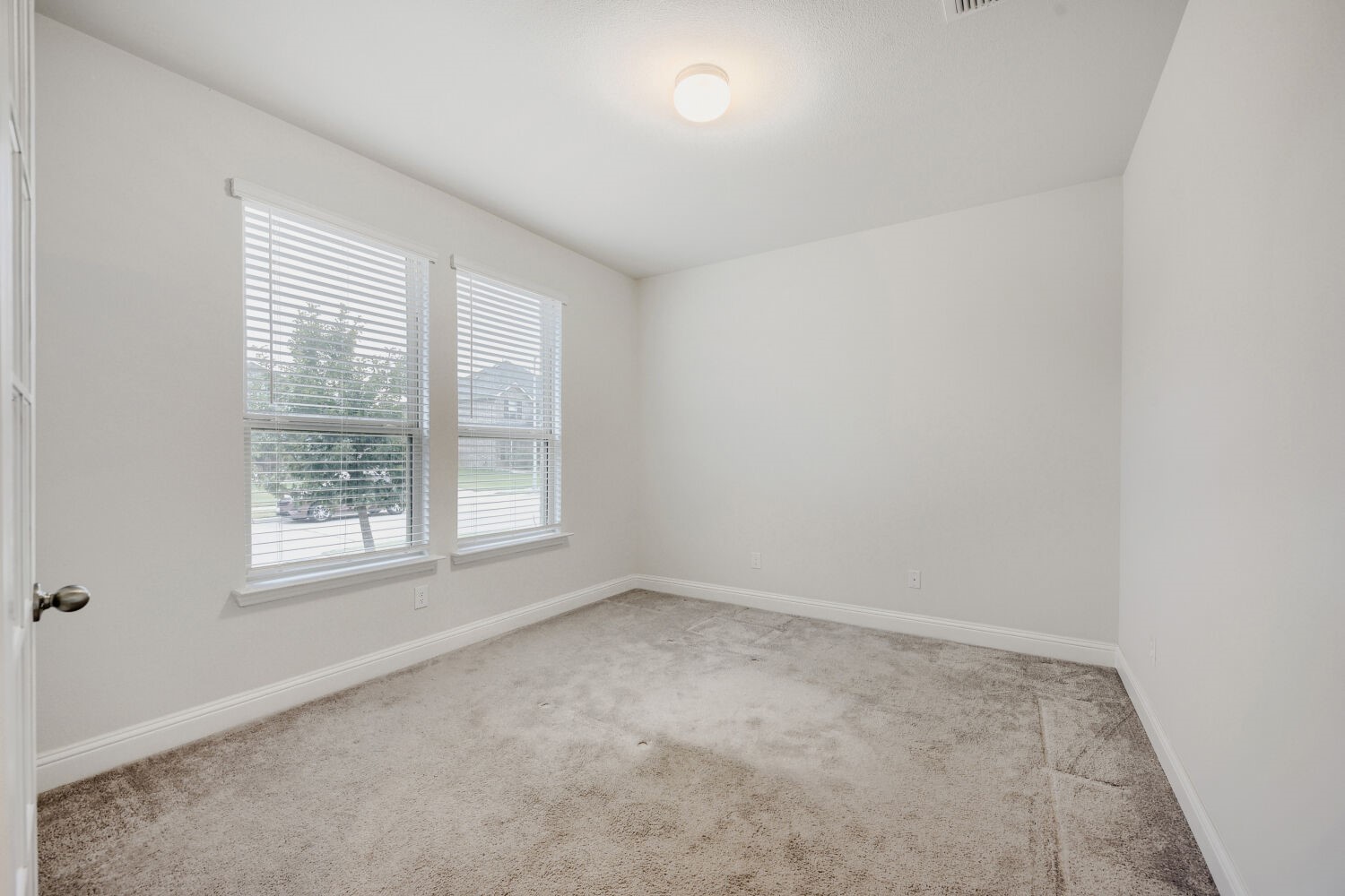 Empty carpeted bedroom with two windows and white blinds.