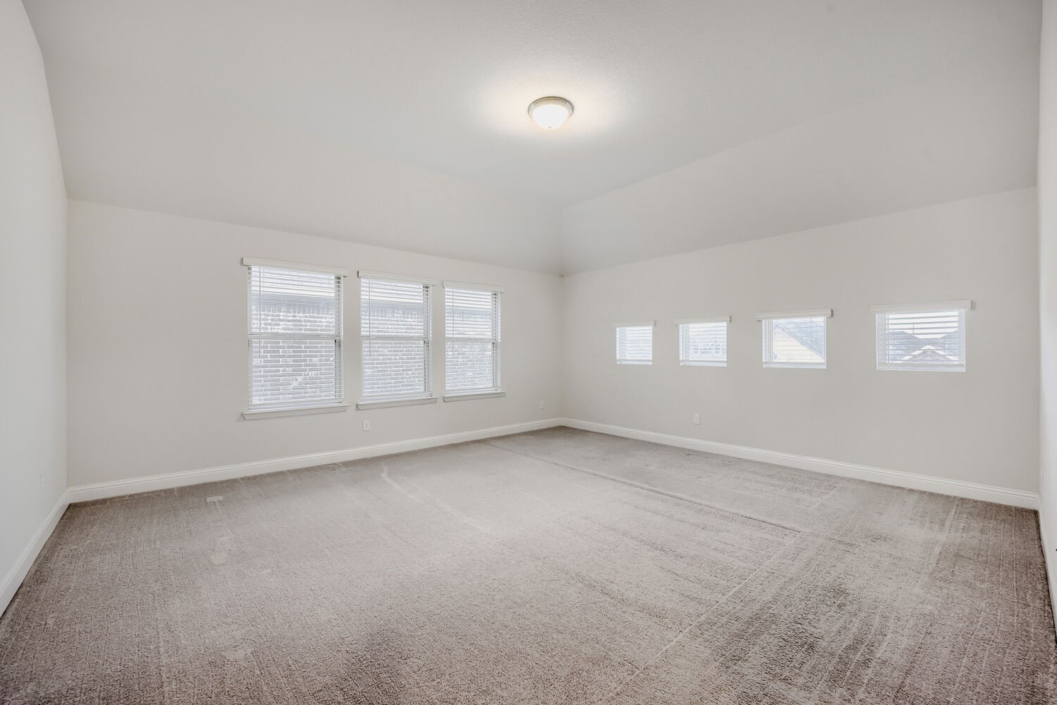 Empty carpeted room with a high ceiling and windows along two walls.