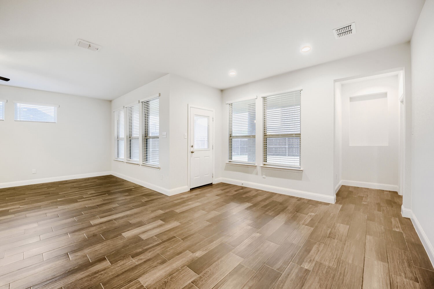 Empty open living area with wood-look tile flooring, multiple windows, and a door.